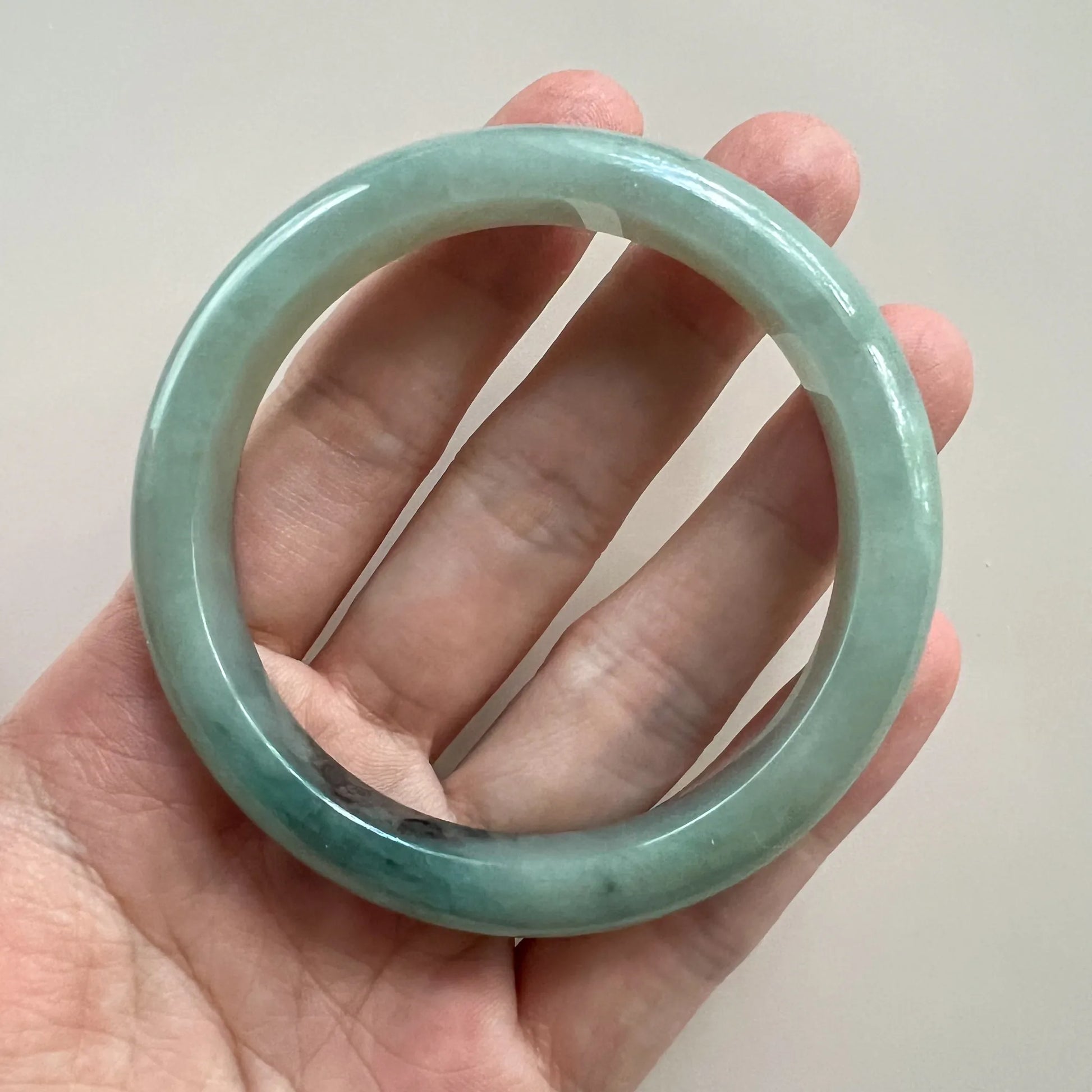 Handheld front view of translucent green jade bangle with polished surface