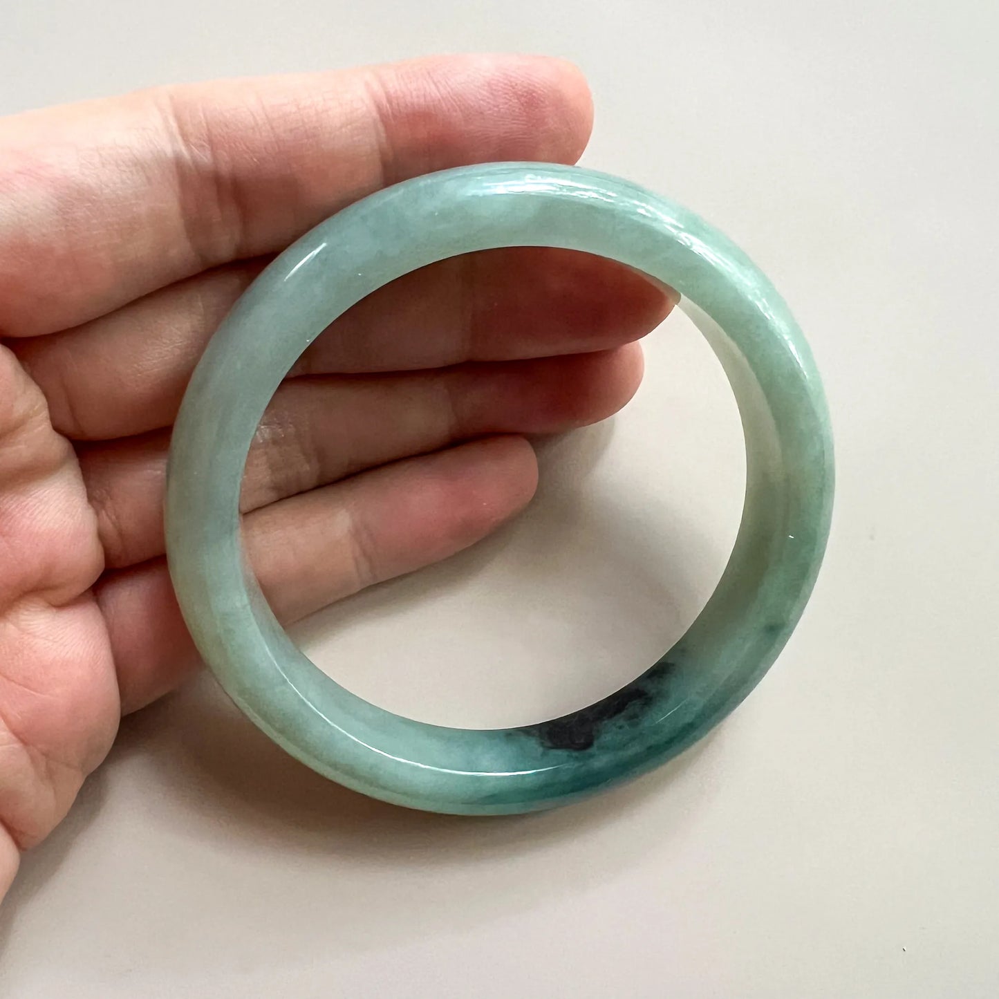 Handheld view of round jade bangle showing dark natural inclusion and glossy finish
