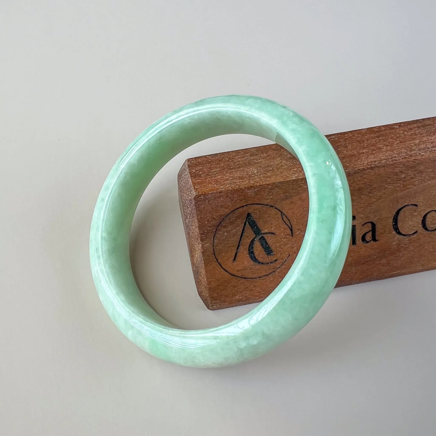 Front view of glossy pale green jade bangle on wood display stand