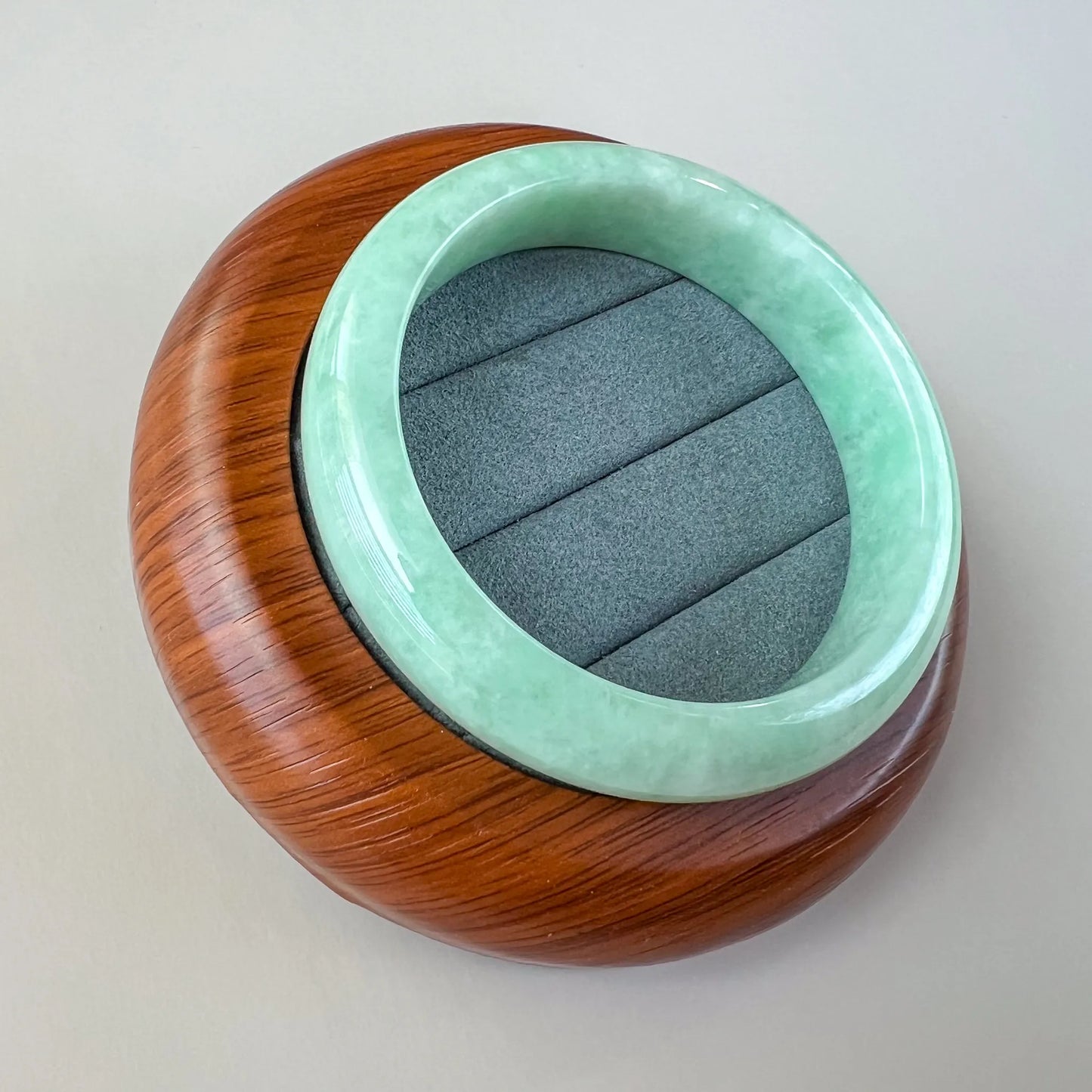 Angled view of smooth mint green jade bangle on wood display stand