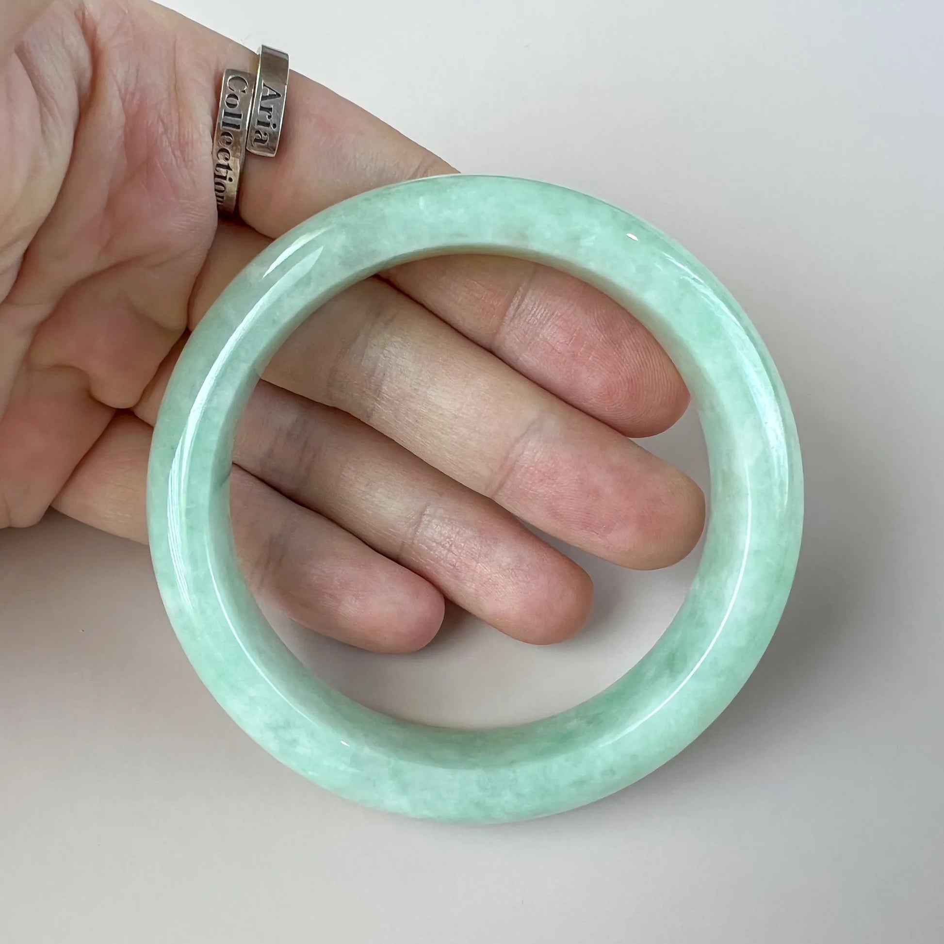Handheld view of polished pale green jade bangle showing rounded profile