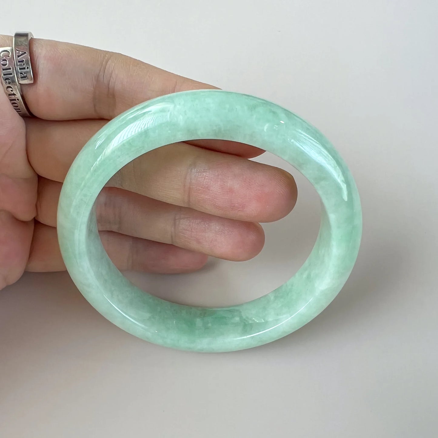 Close handheld view of glossy light green jade bangle with translucent finish