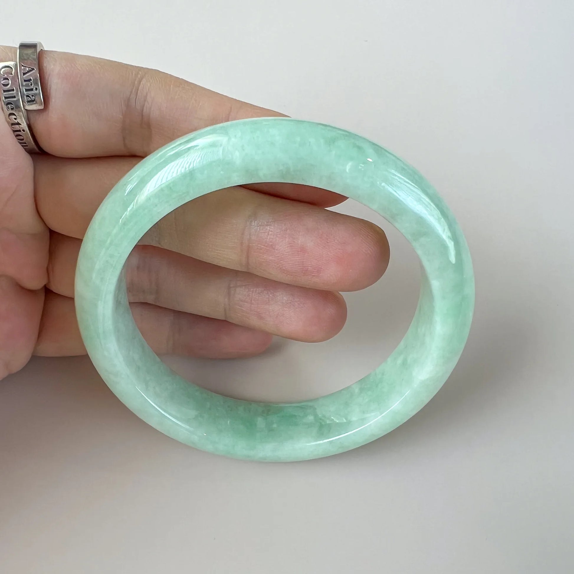 Close handheld view of glossy light green jade bangle with translucent finish