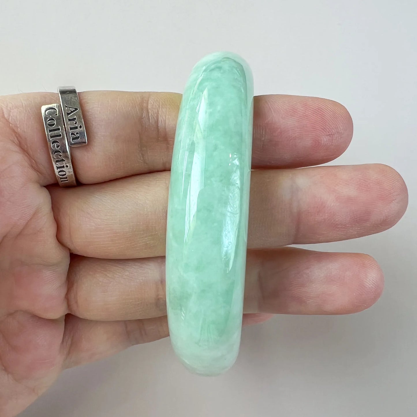 Narrow side view of polished light green jade bangle with rounded edges