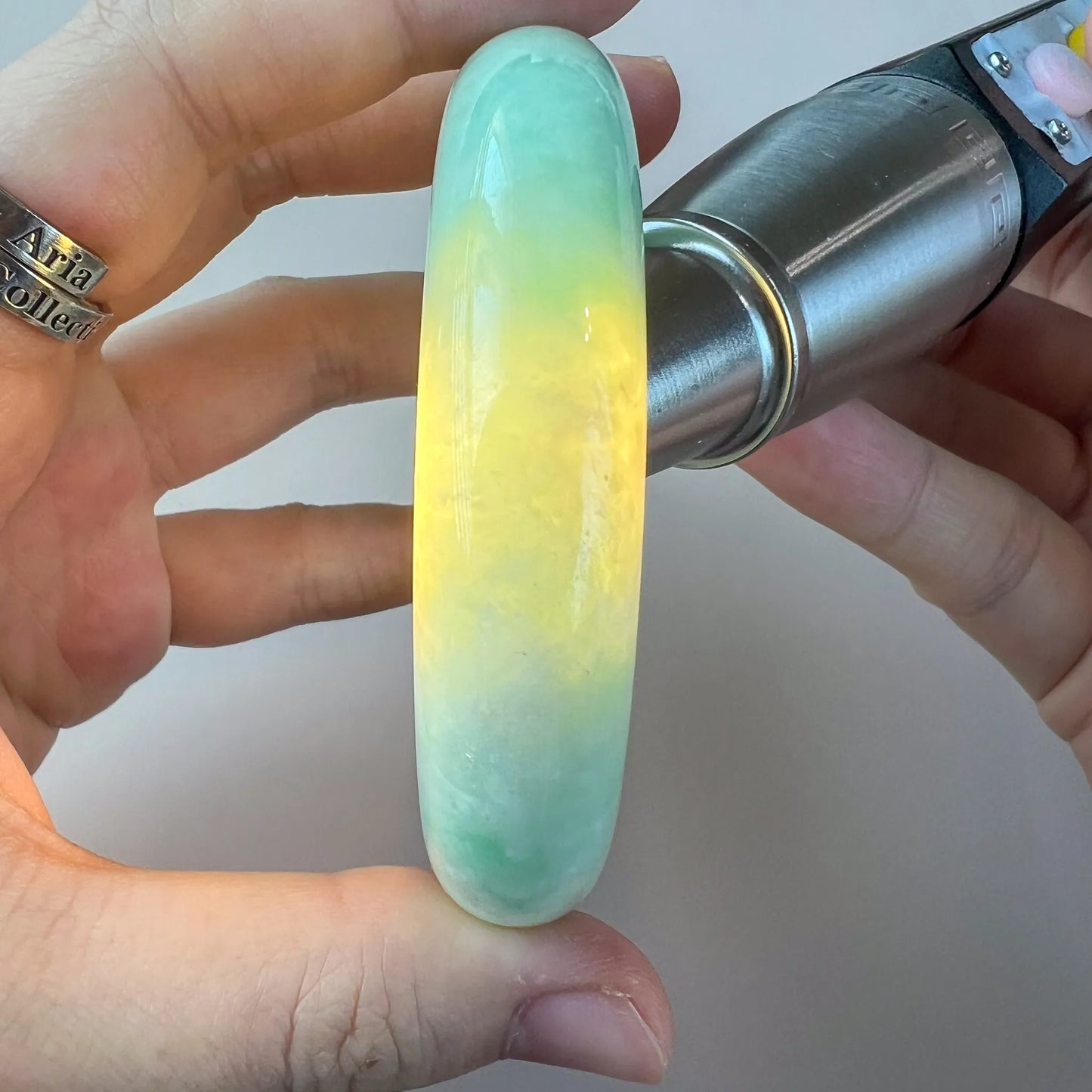 Handheld jade bangle under light showing natural color zoning and glossy finish