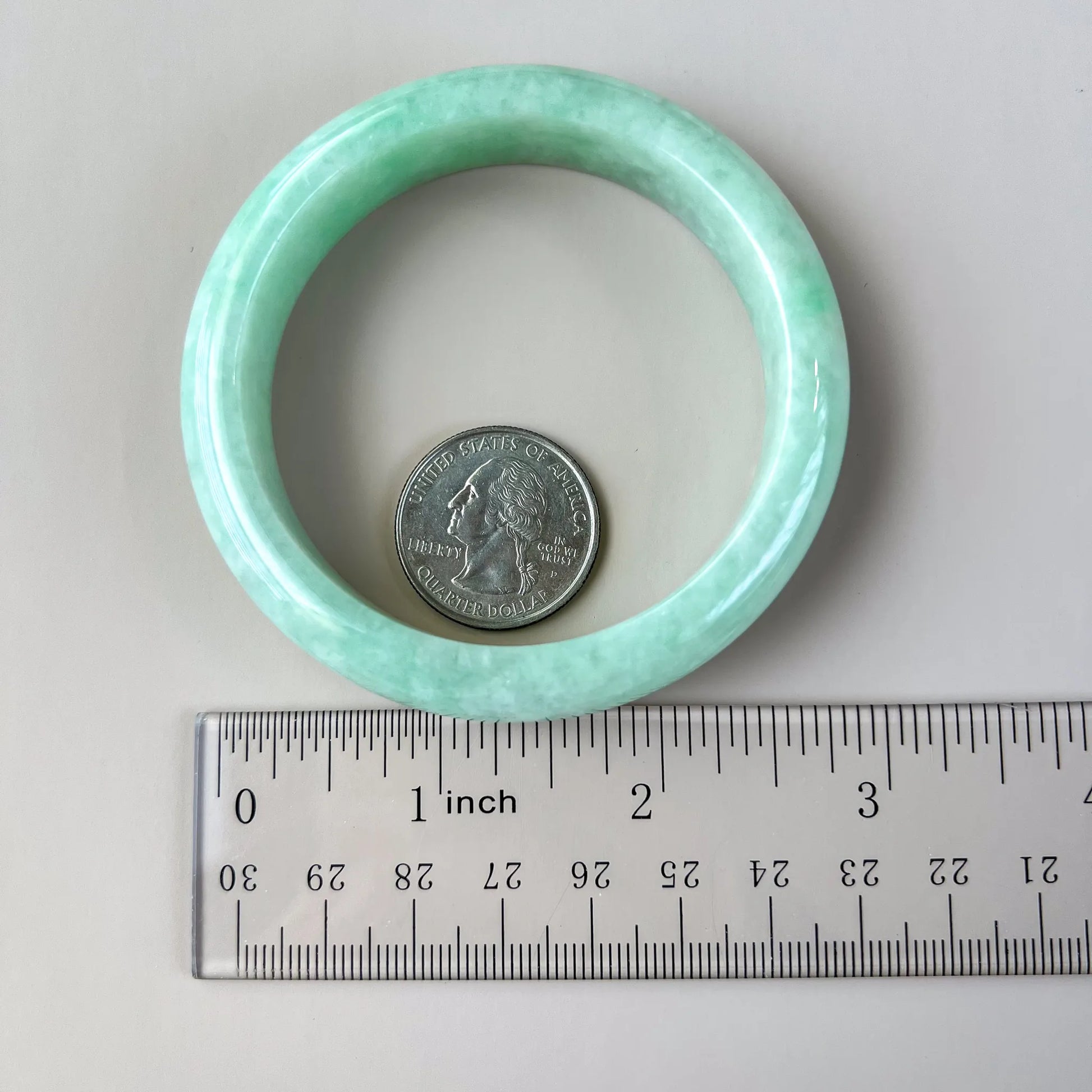 Light green natural jade bangle shown with ruler and quarter for scale, polished rounded profile
