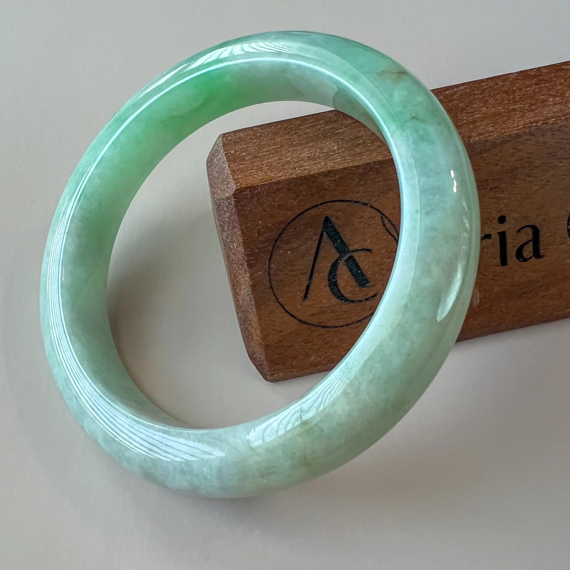 Light green Burmese Type A jadeite jade bangle angled on wooden stand, glossy polished finish with subtle marbling