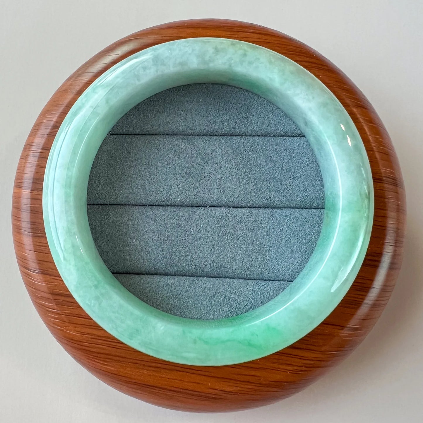 Top-down view of light green Burmese Type A jadeite jade bangle with glossy finish on wooden display stand