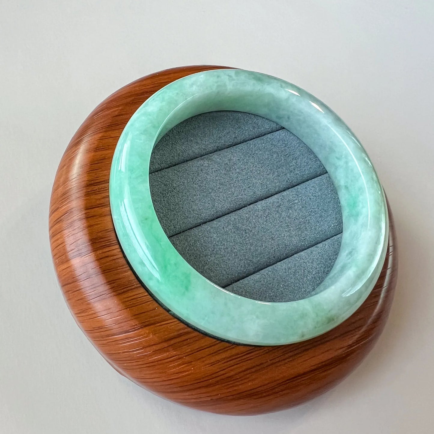 Top-down close-up of light green jadeite bangle with glossy finish on a wooden display stand and gray cushion