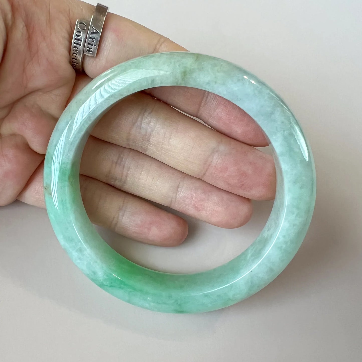Close-up of light green Burmese Type A jadeite jade bangle with glossy finish and natural mottled texture in hand