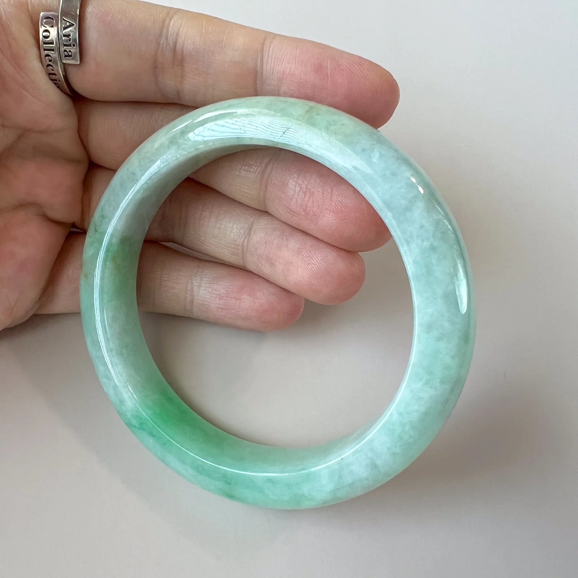 Light green Burmese Type A jadeite jade classic bangle, glossy polished finish, held in hand at close-up angle