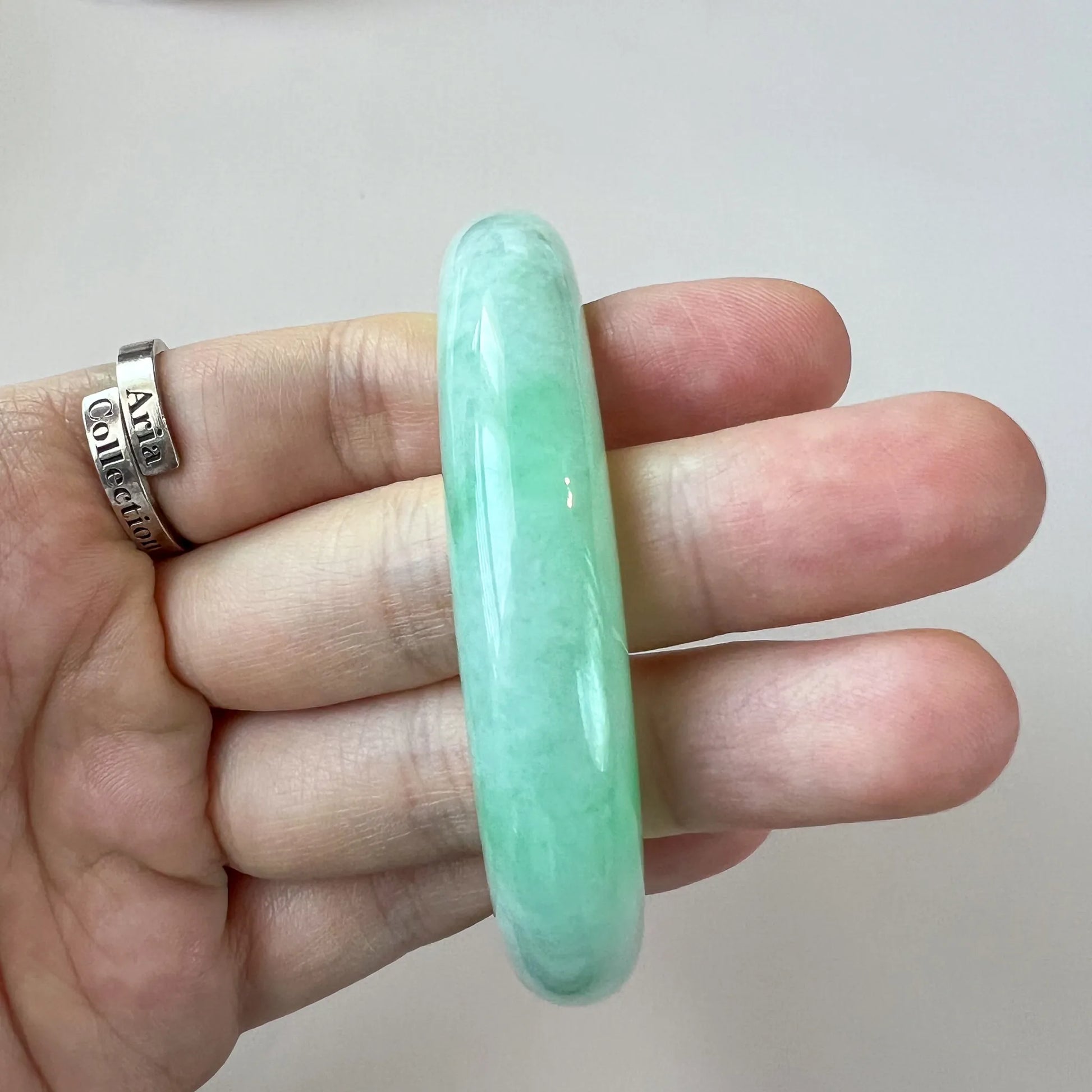 Close-up of light green jadeite bangle held in hand, showing polished translucent finish and smooth rounded profile