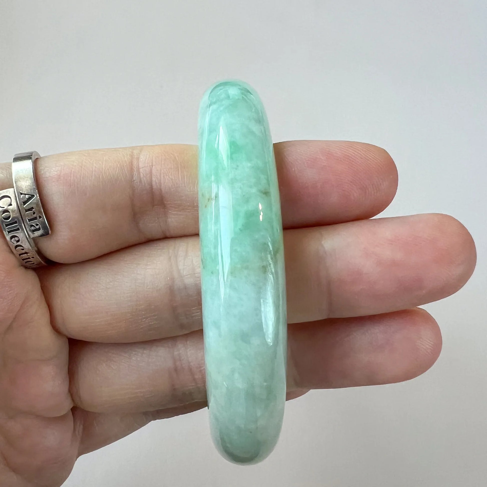 Close-up of light green jadeite jade bangle held in hand, polished glossy finish with translucent cloudy texture