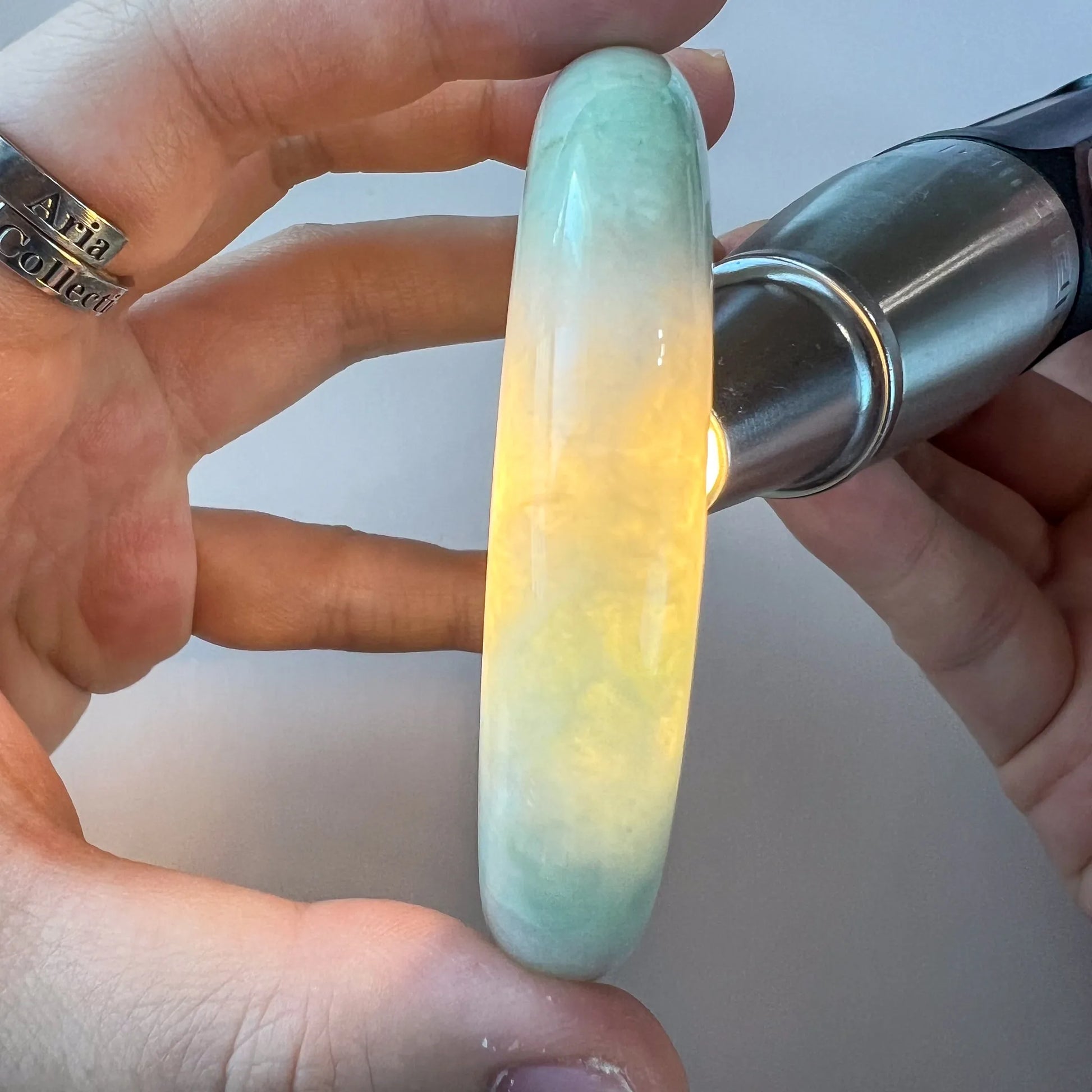 Close-up side view of a polished light green Burmese type A jadeite jade bangle glowing under backlight in hand
