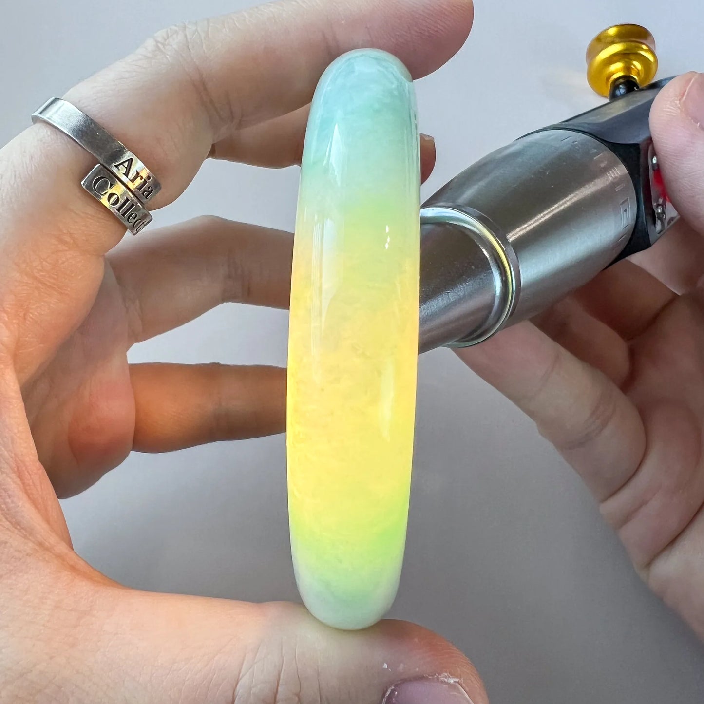Close-up of a polished light green Burmese Type A jadeite jade bangle held in hand under bright light, showing translucency