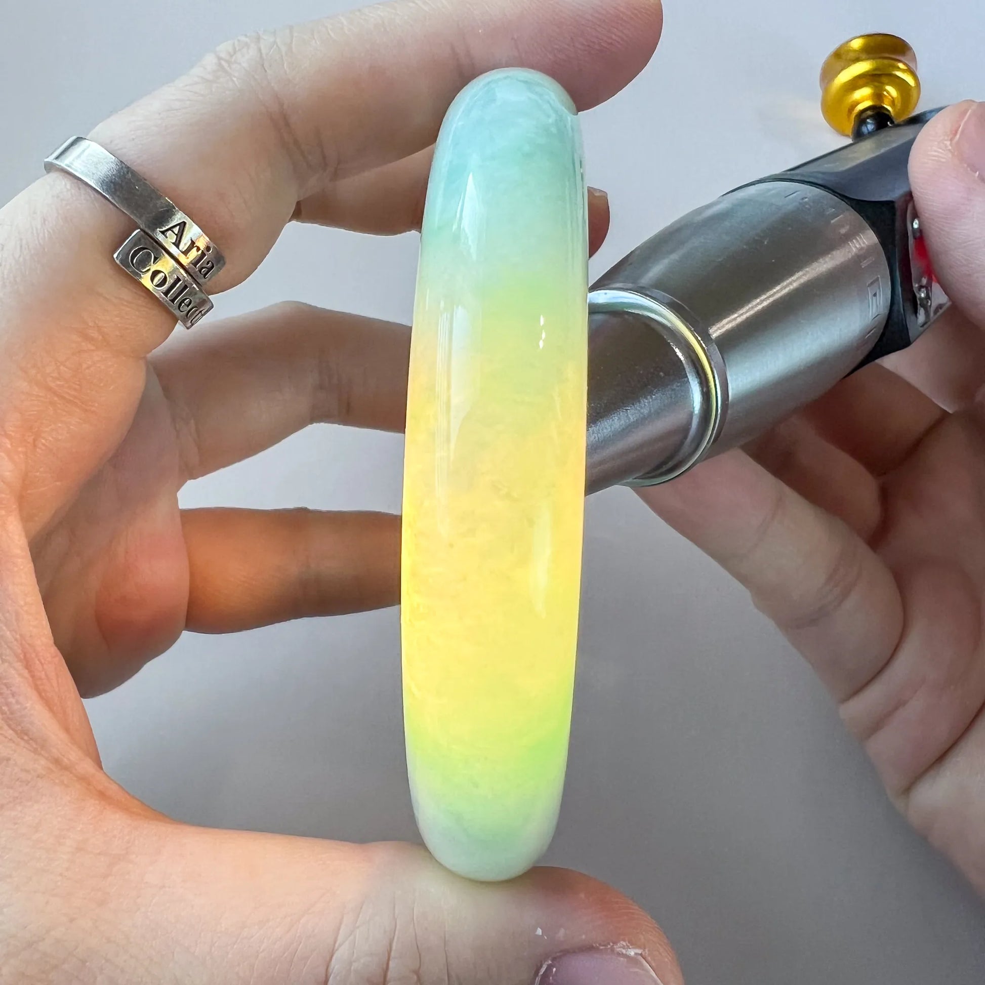 Close-up of a polished light green Burmese Type A jadeite jade bangle held in hand under bright light, showing translucency