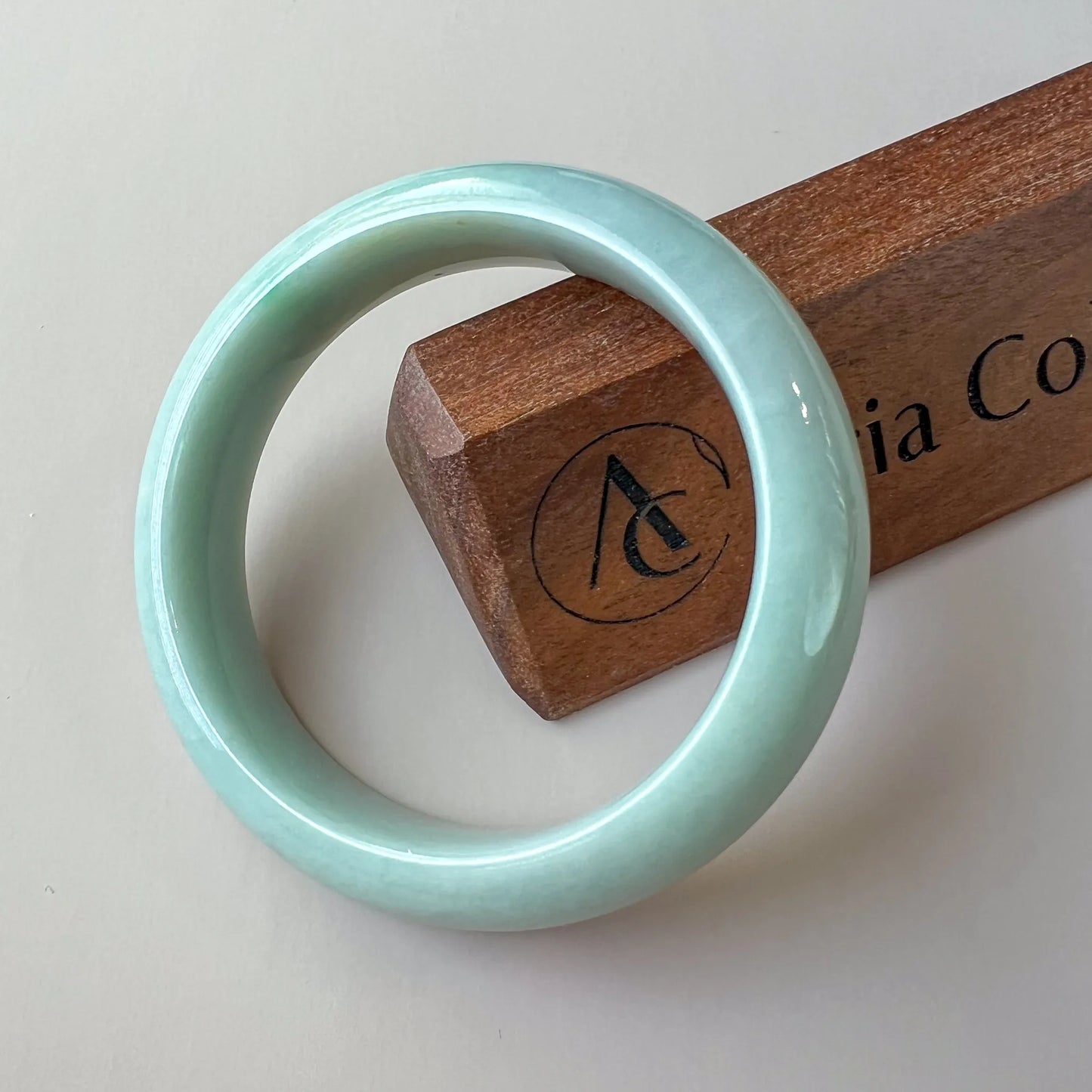 Glossy pale green jade bangle resting on a wooden display block, front angled view