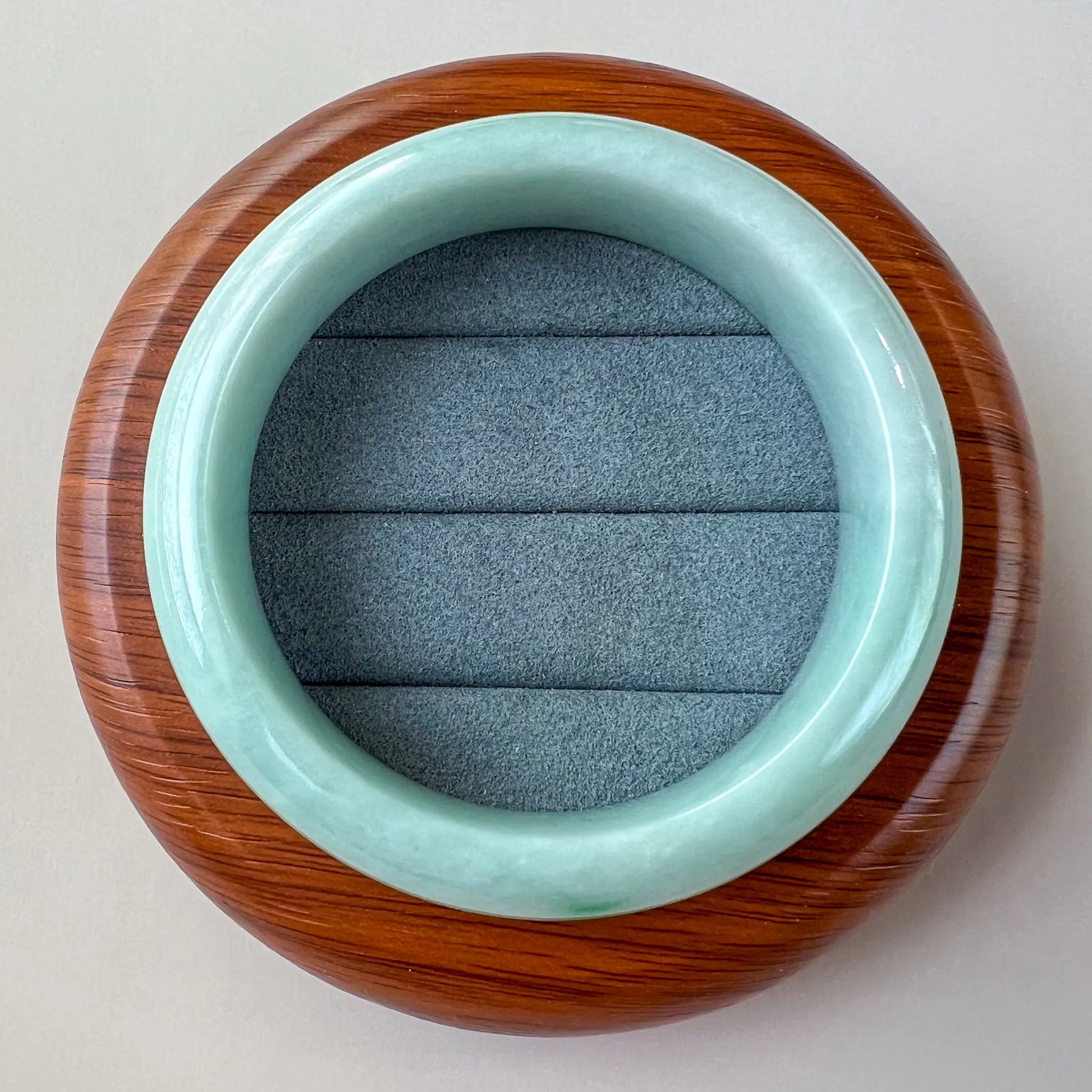 Top-down view of polished jade bangle on round wooden stand with padded insert