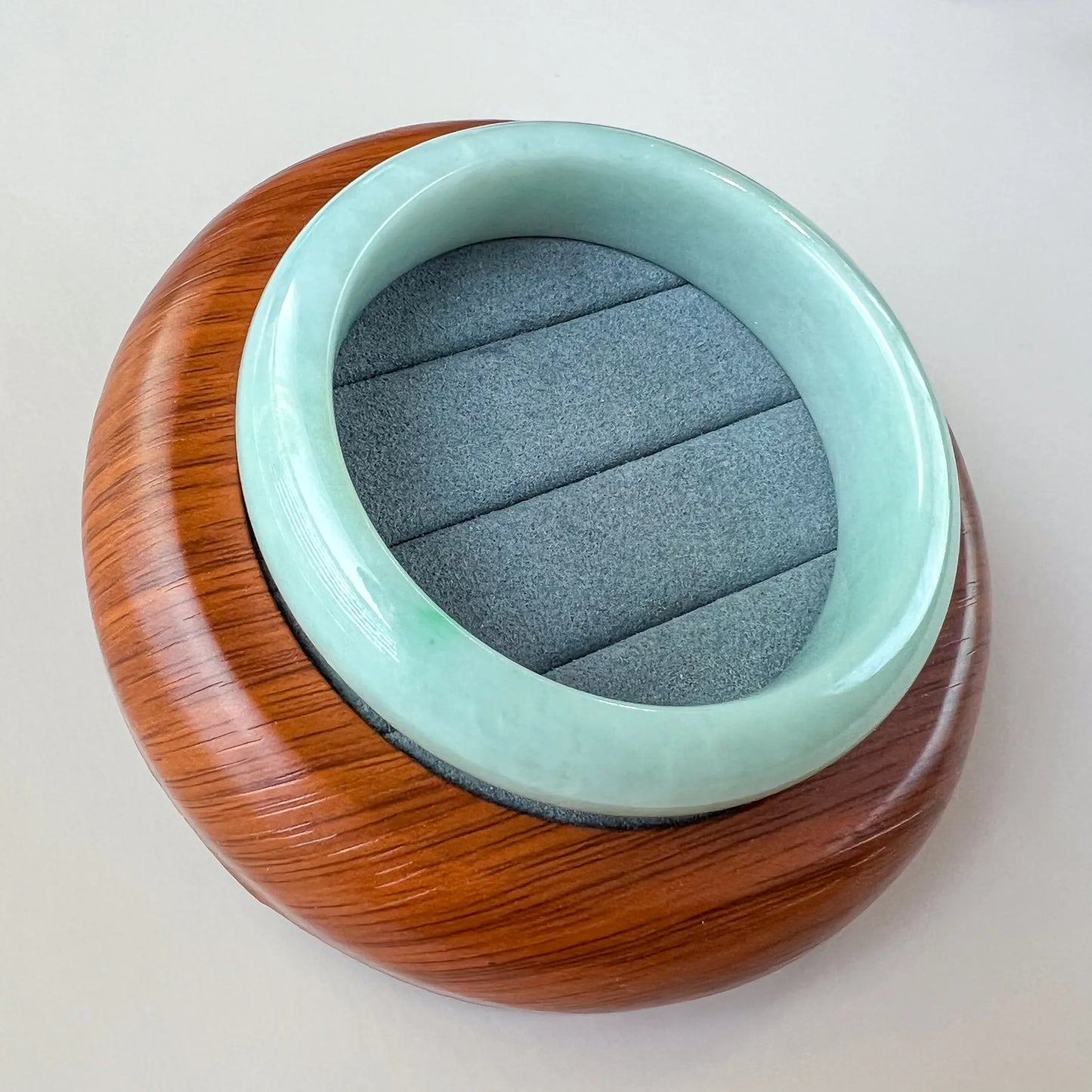 Angled overhead view of smooth light green jade bangle on wood presentation base