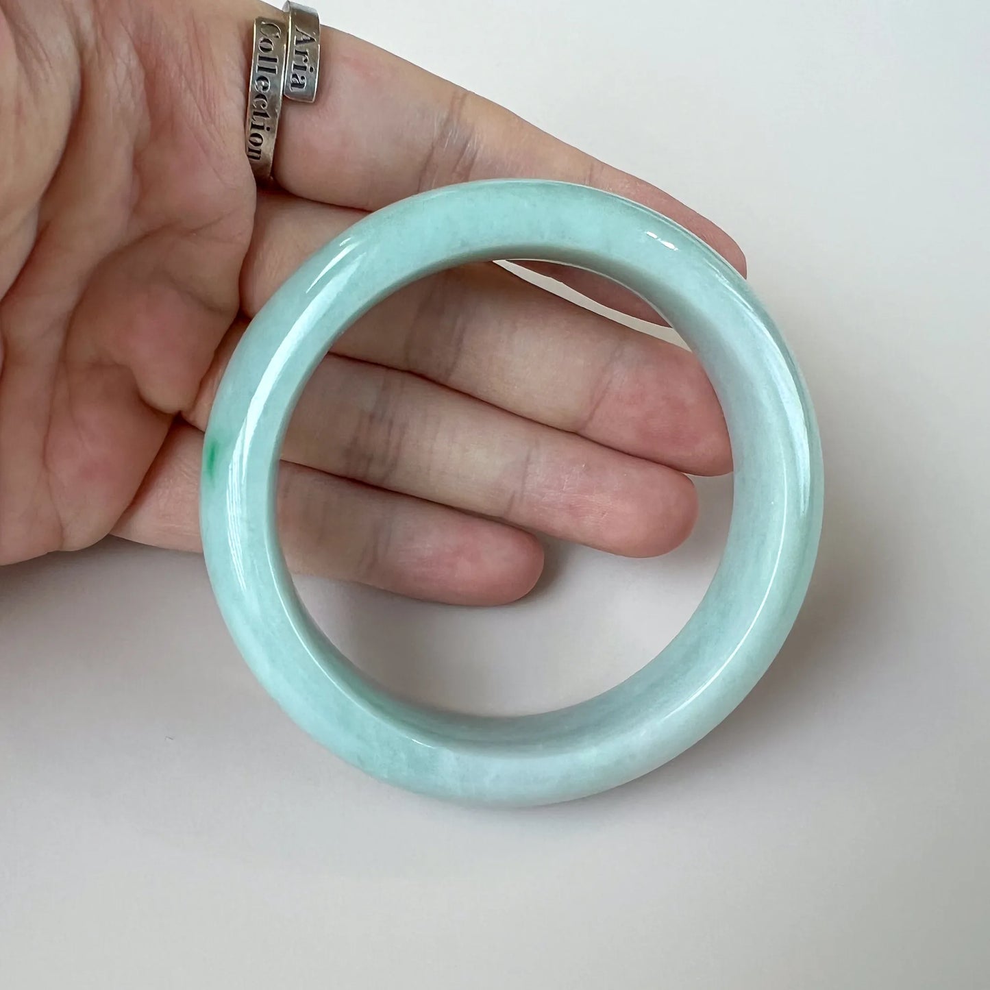 Handheld view of polished pale green jade bangle showing smooth rounded profile