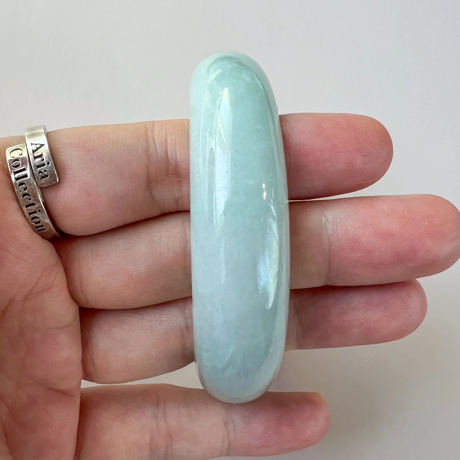 Side profile of glossy light green jade bangle held in hand, translucent stone finish