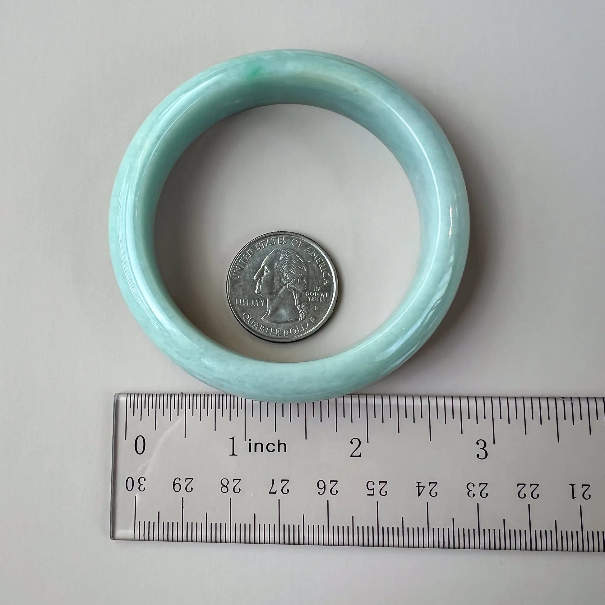 Top view of light green natural jade bangle with ruler and quarter for scale, showing rounded profile