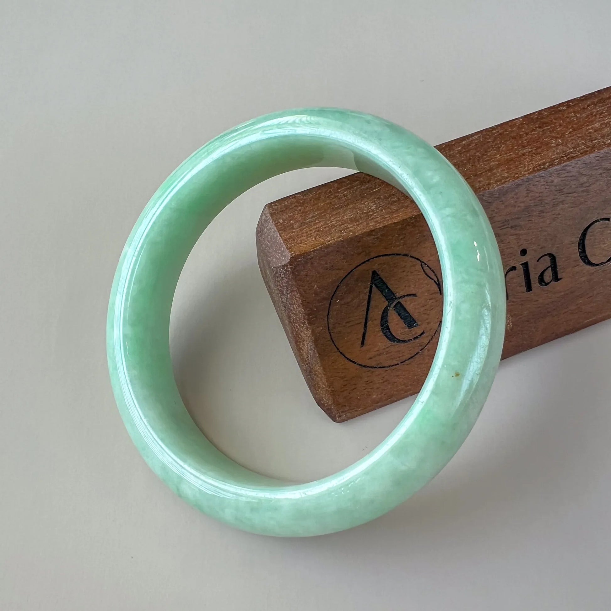 Front view of polished pale green jade bangle on display stand