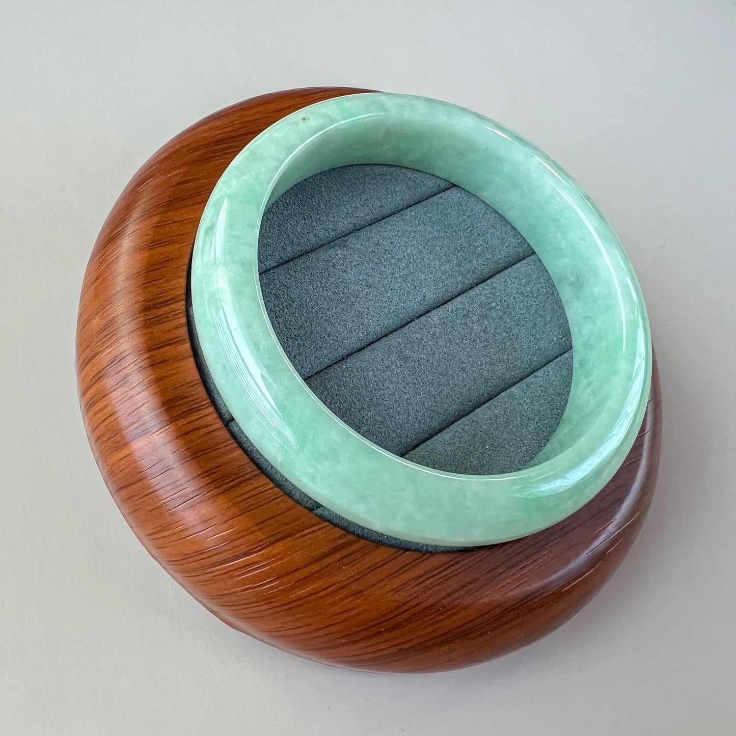Angled view of smooth green jade bangle on wooden display base