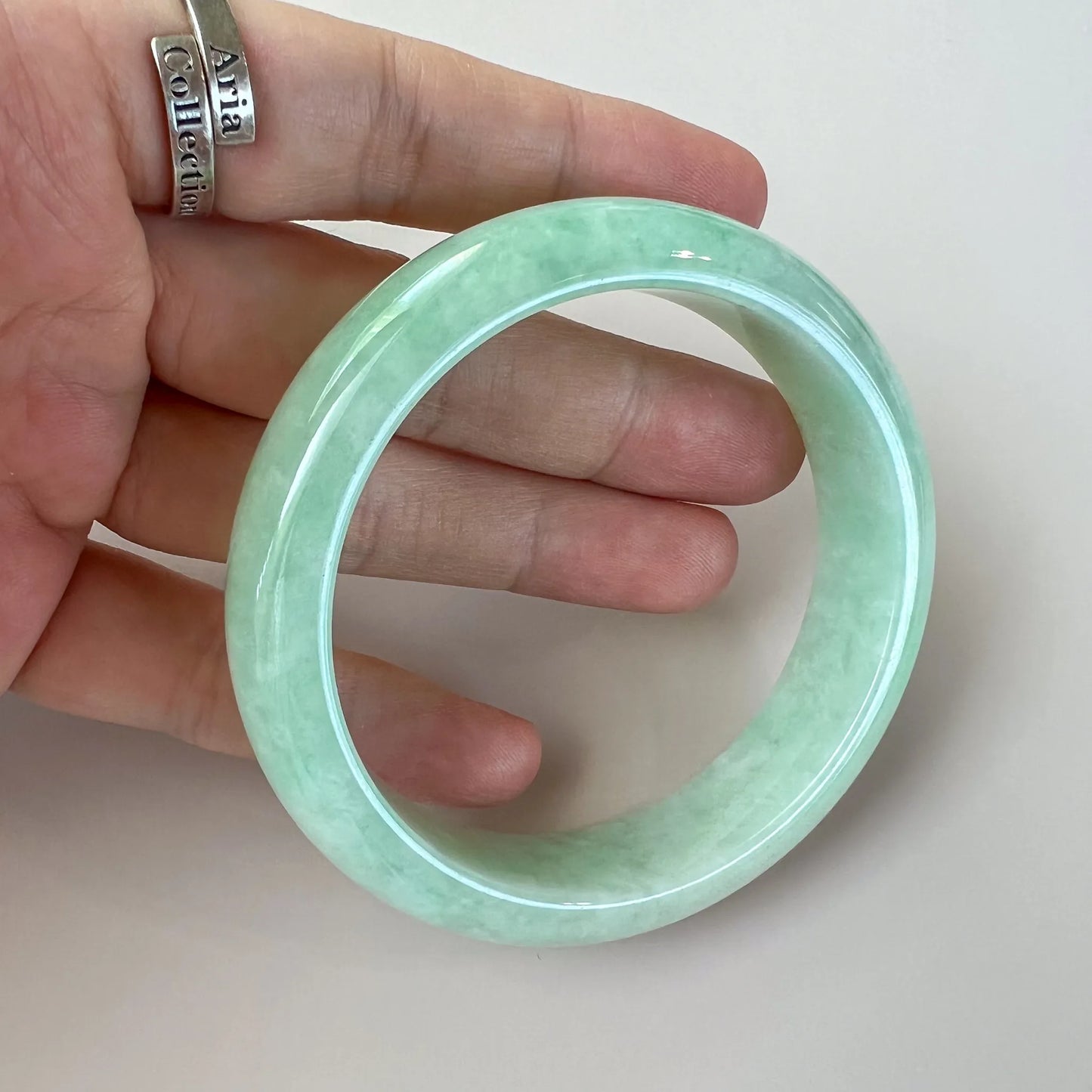 Handheld view of polished light green jade bangle with glossy finish