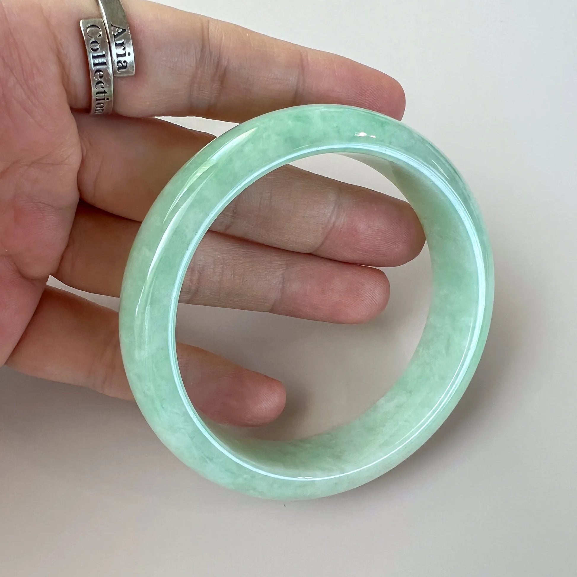 Handheld view of polished light green jade bangle with glossy finish