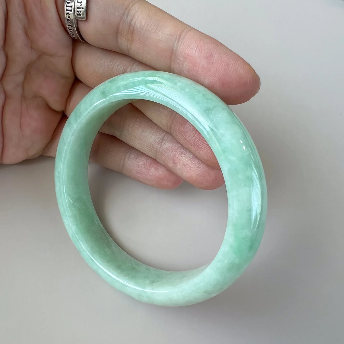 Angled handheld view of smooth pale green jade bangle with natural marbling
