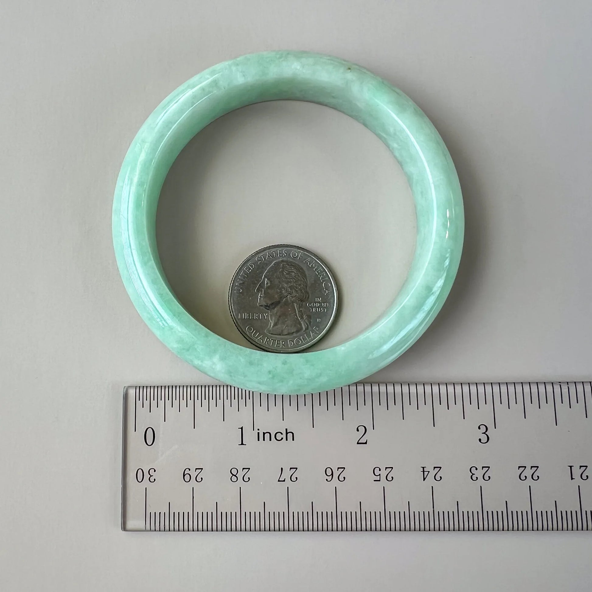 Top view of light green natural jade bangle with ruler and coin showing size and smooth inner surface