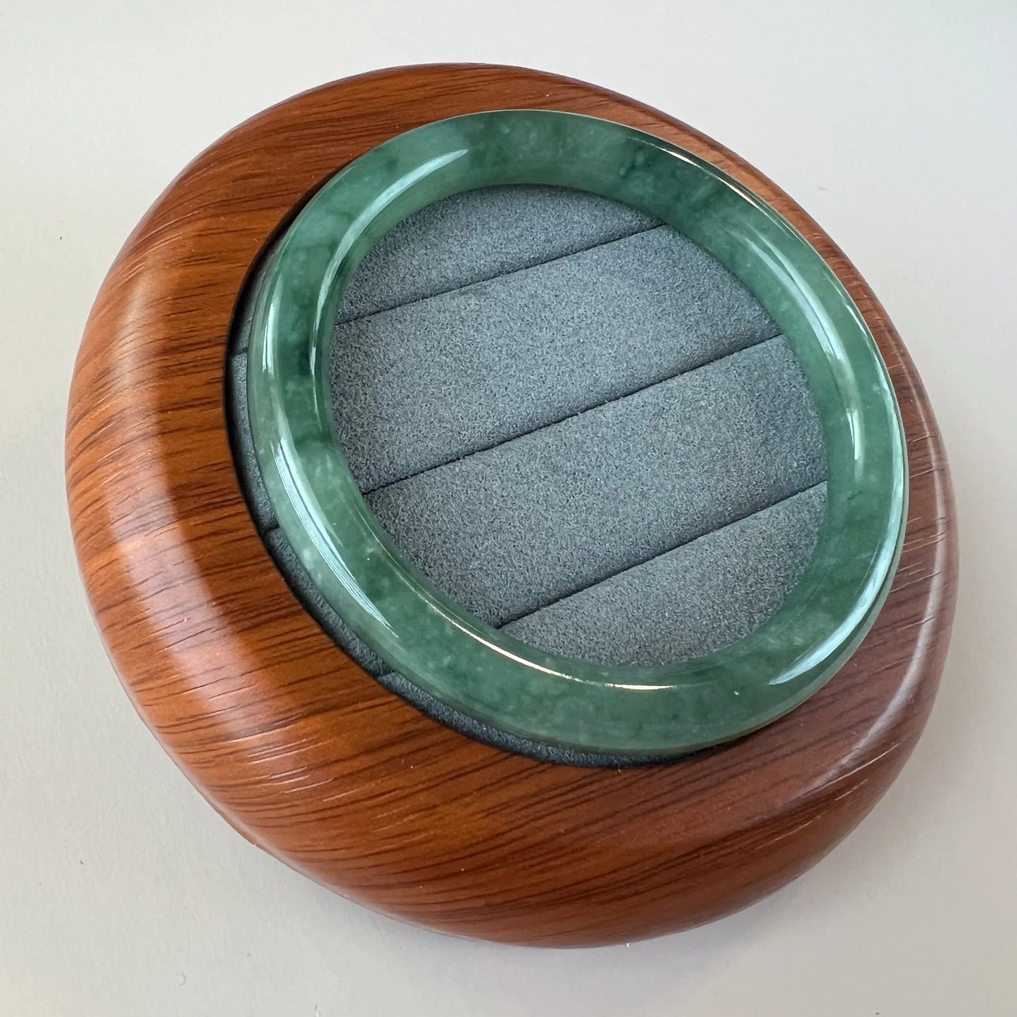 Angled view of glossy green jade bangle in fitted wooden display case