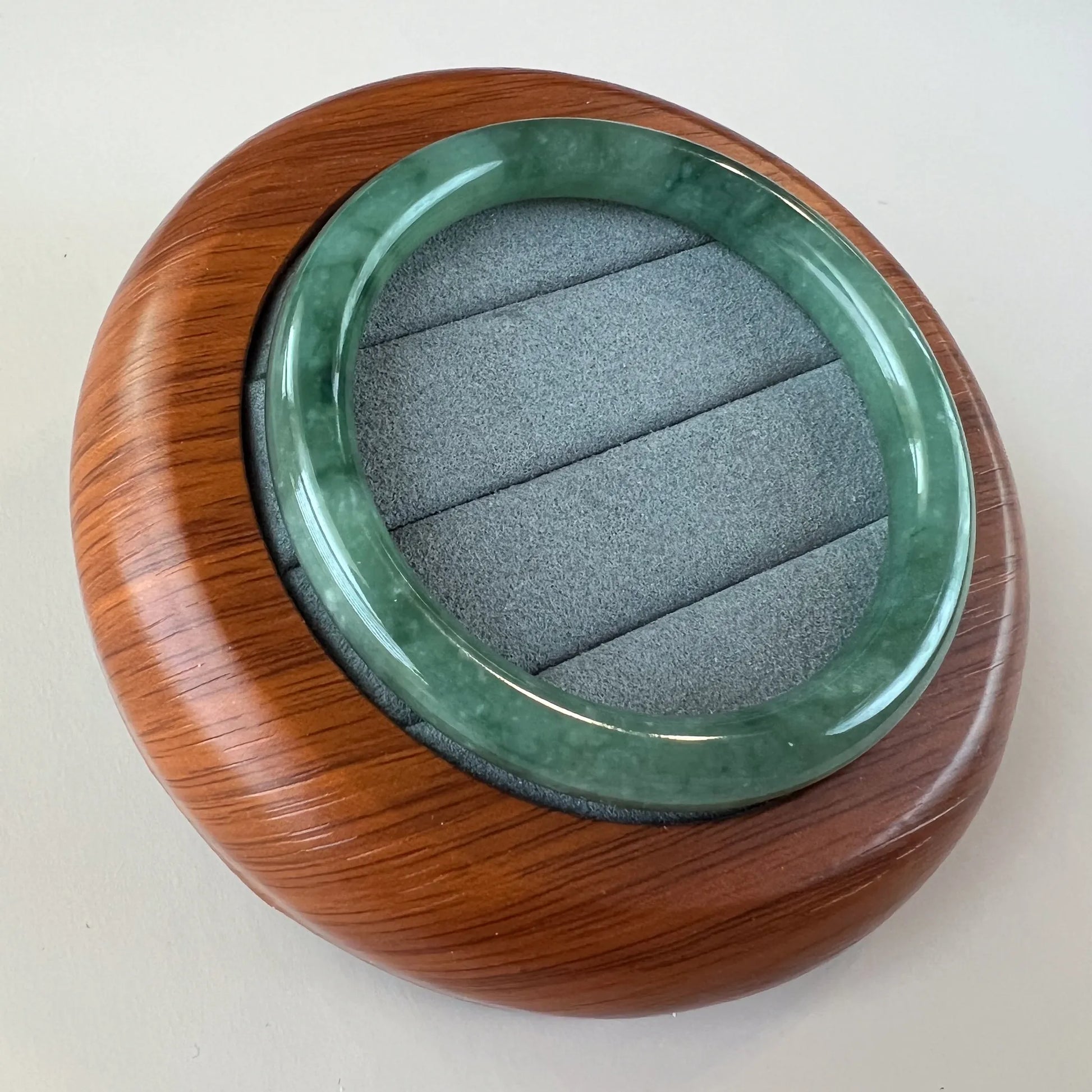 Angled view of glossy green jade bangle in fitted wooden display case