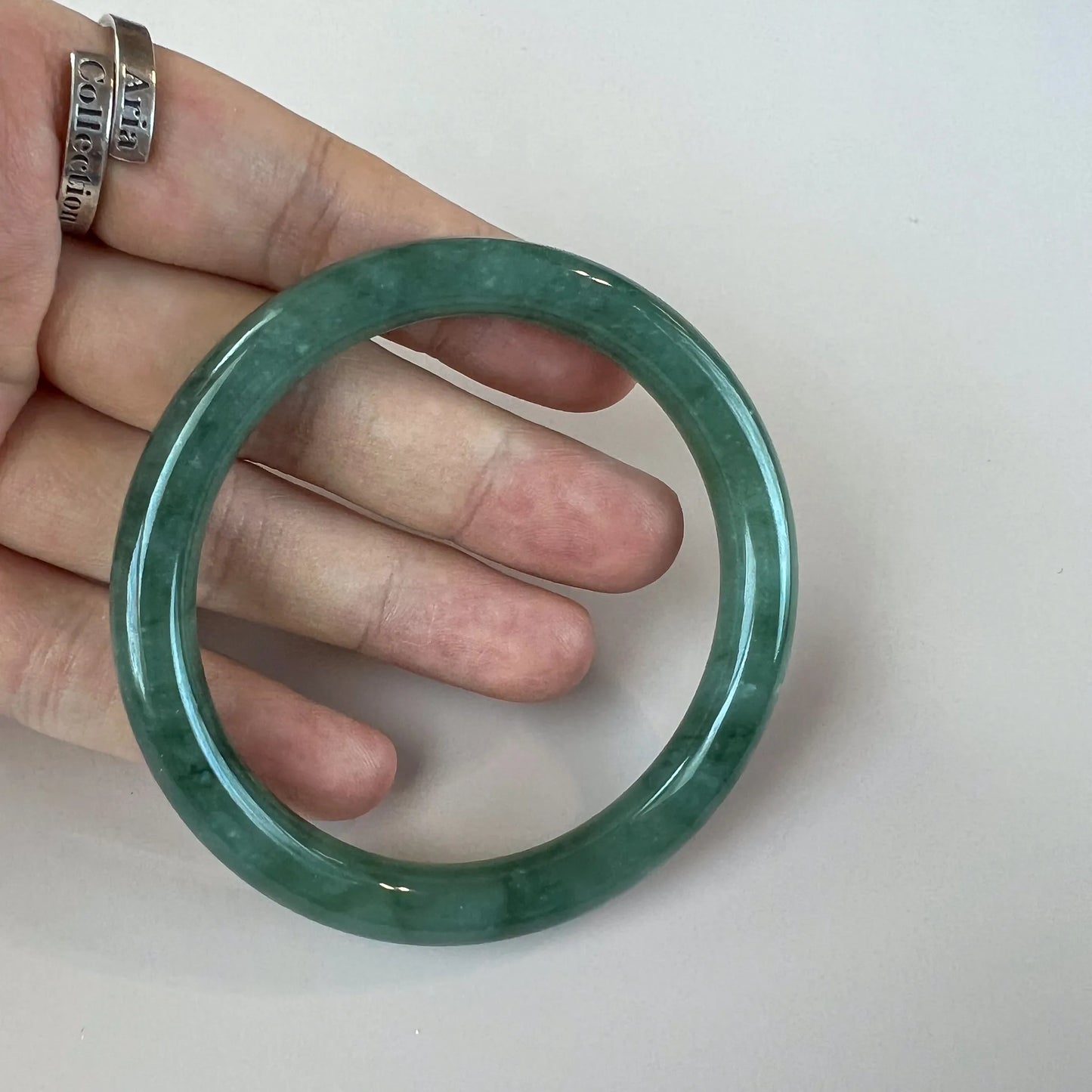 Hand-held front view of smooth green jade bangle with polished finish