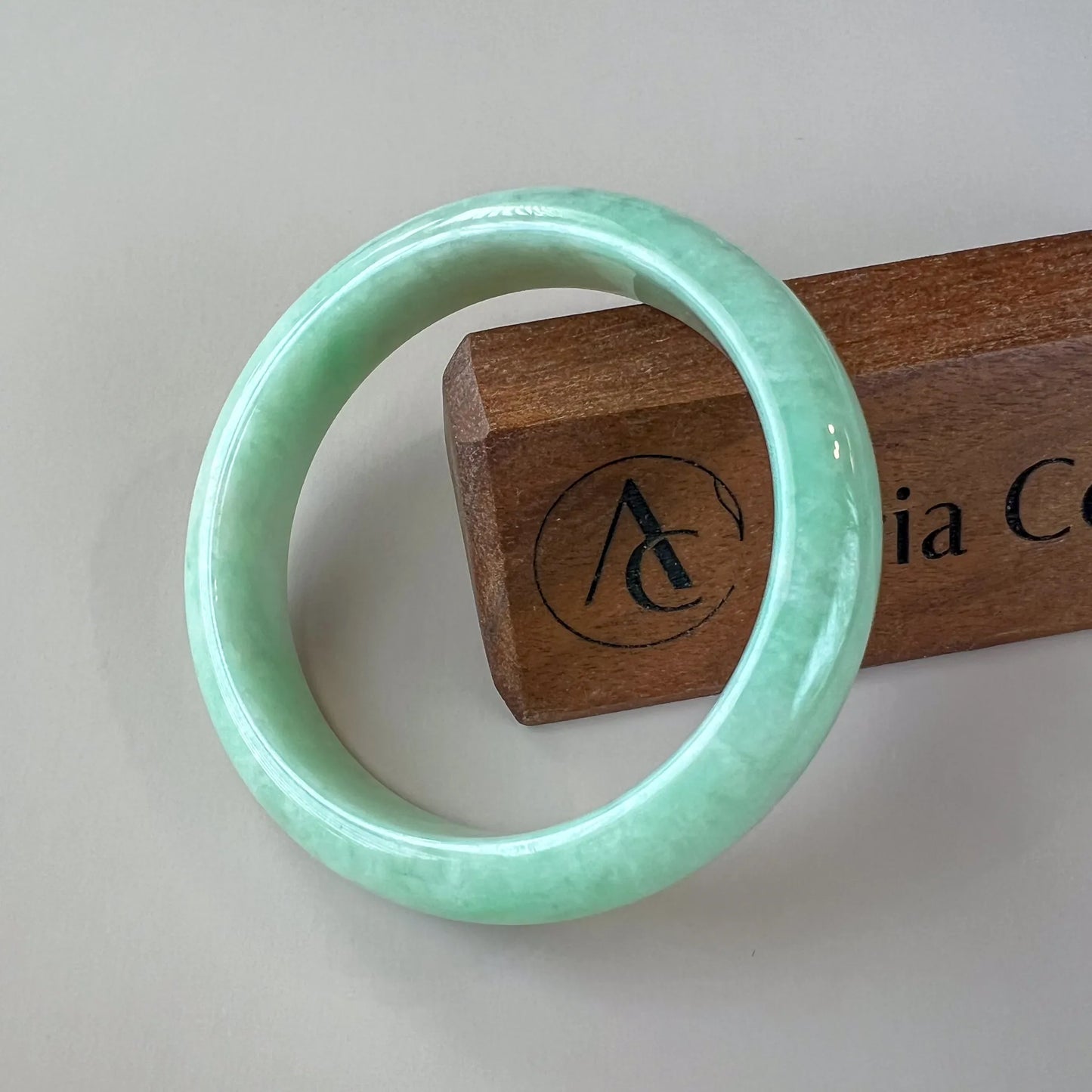 Glossy green jade bangle front view on neutral background with wooden stand