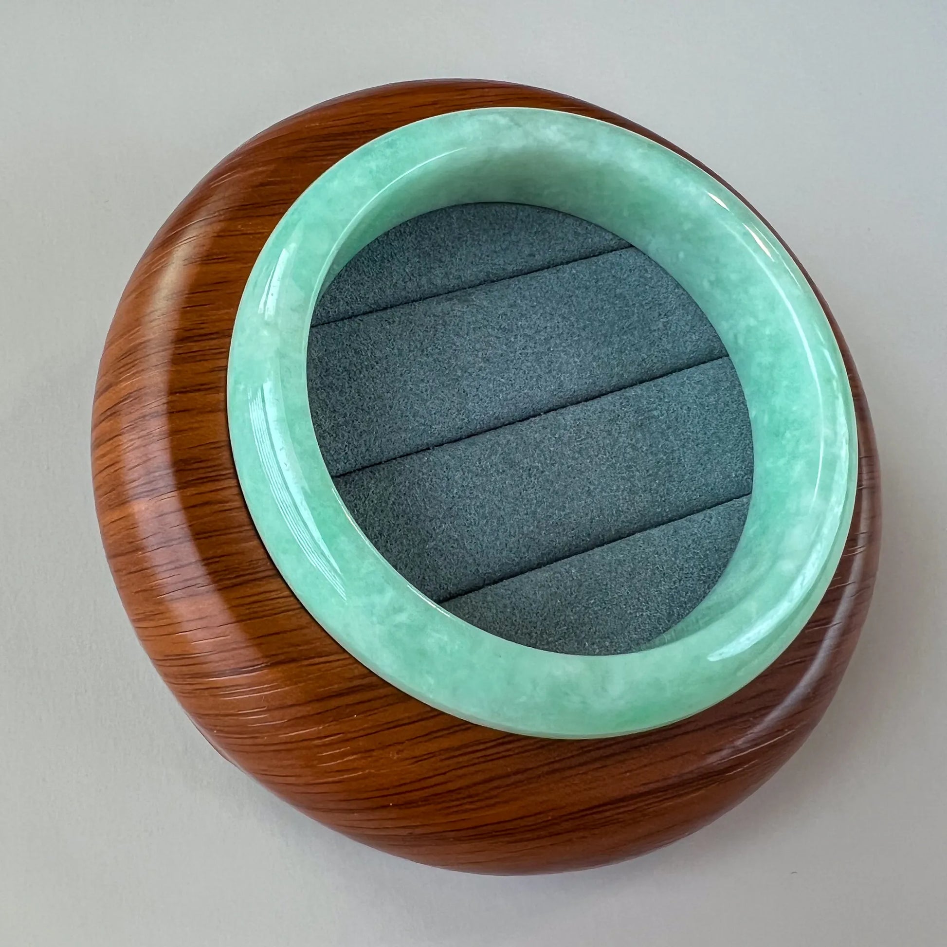 Angled overhead view of mint green jade bangle in round wooden case