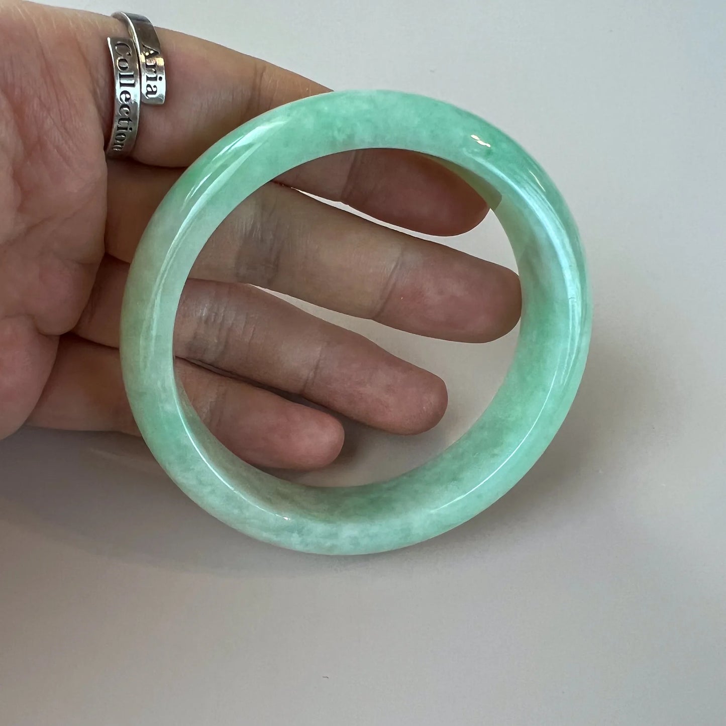Handheld view of smooth green jade bangle showing rounded profile and polished finish
