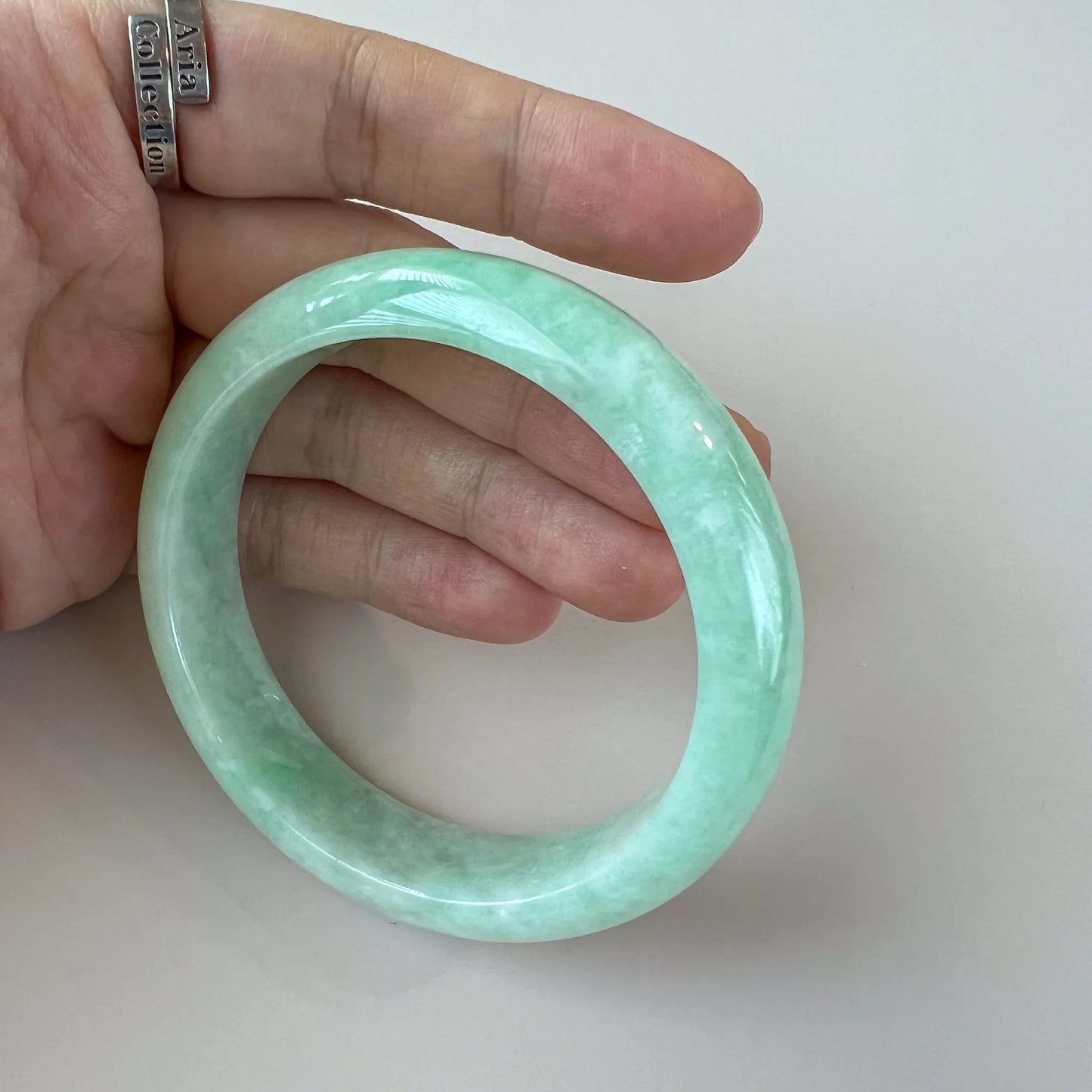 Handheld angled view of translucent jade bangle with glossy polished surface