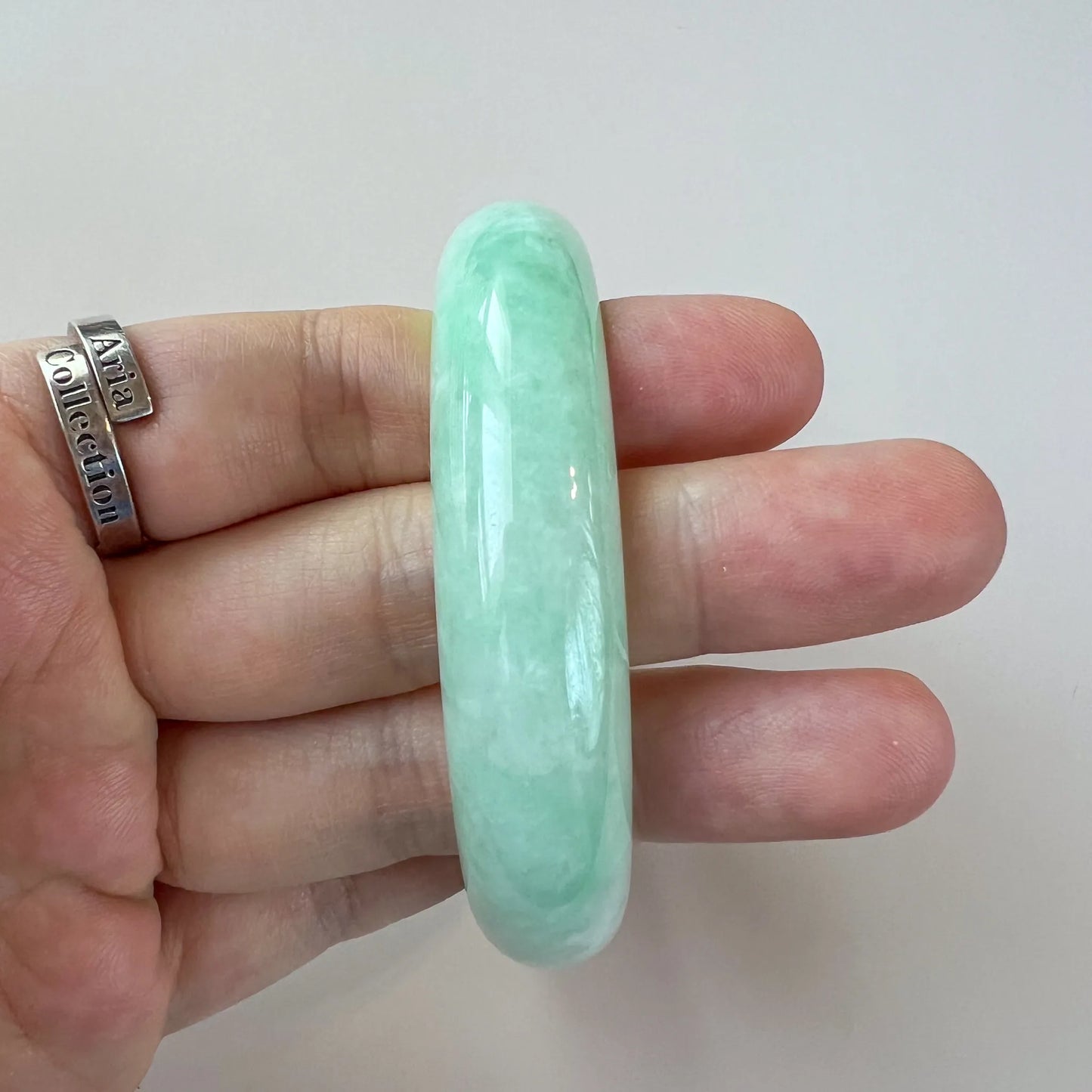 Side profile of smooth light green jade bangle held in hand