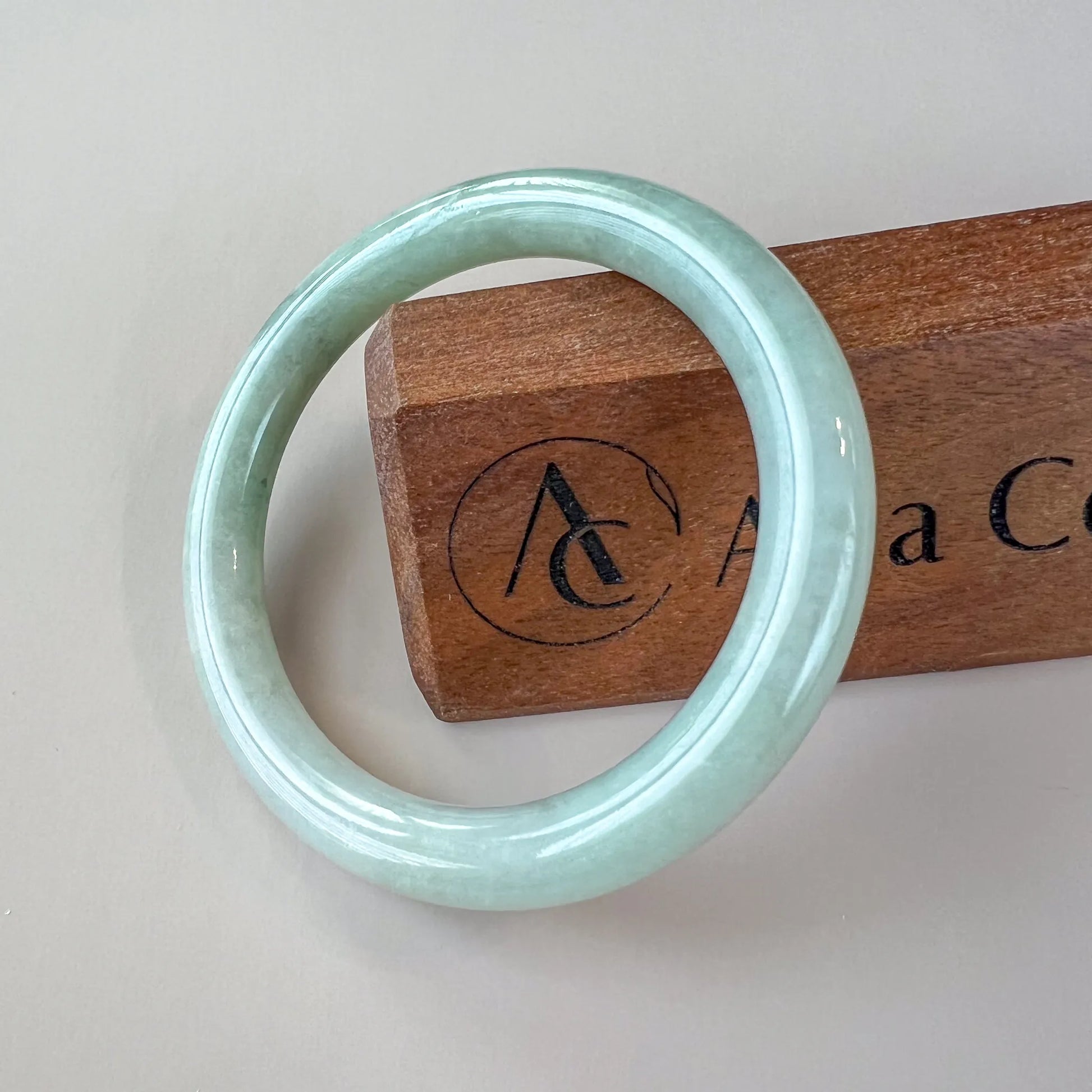 Front view of polished pale green jade bangle on neutral background