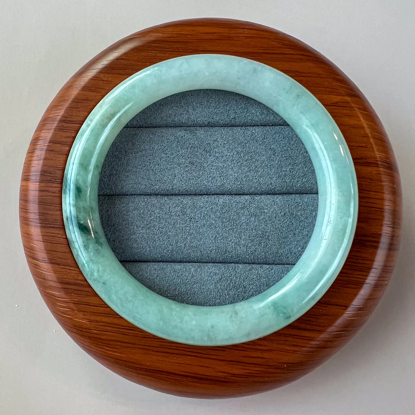 Top-down view of glossy jade bangle on round wooden display stand