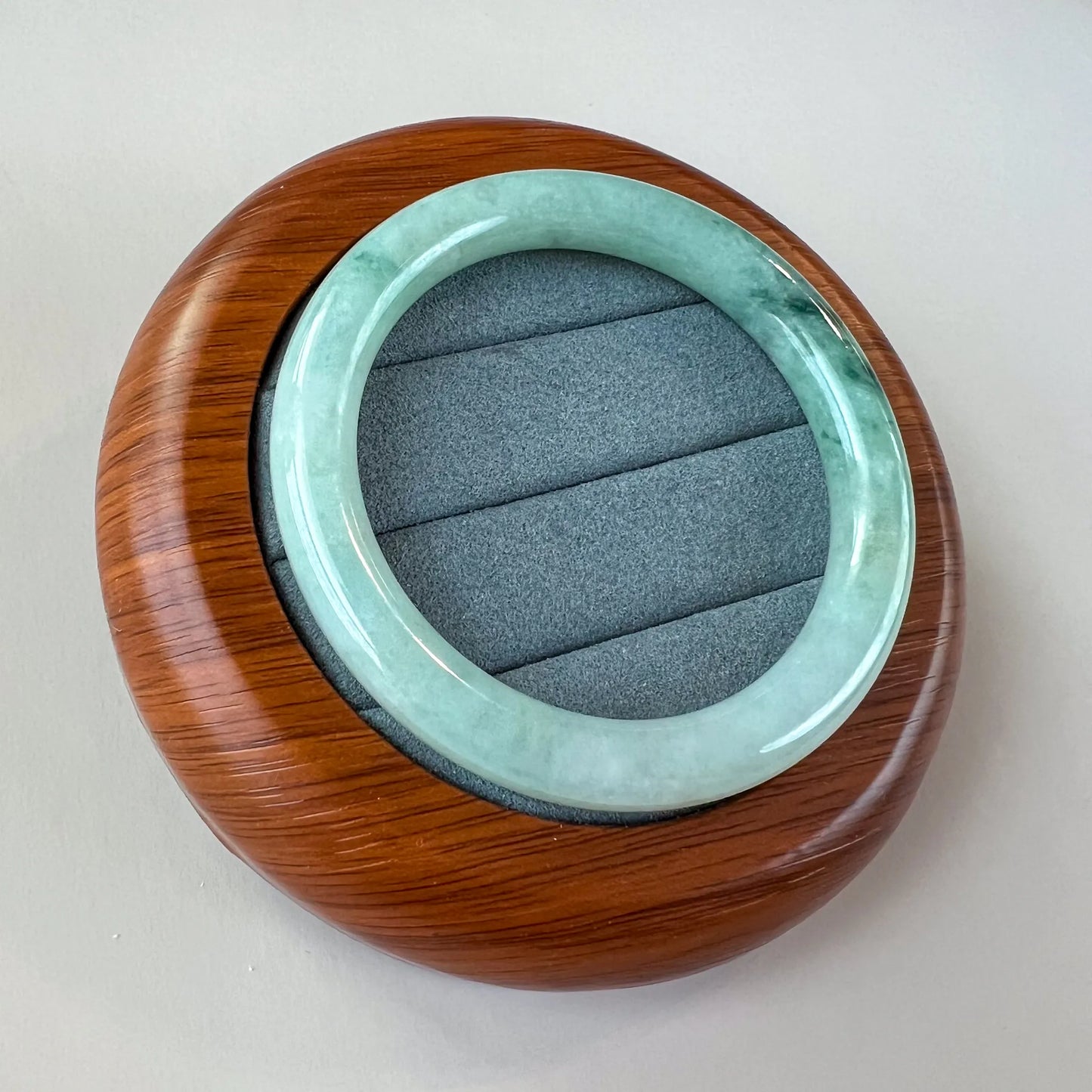 Angled view of smooth jade bangle resting on wooden presentation stand