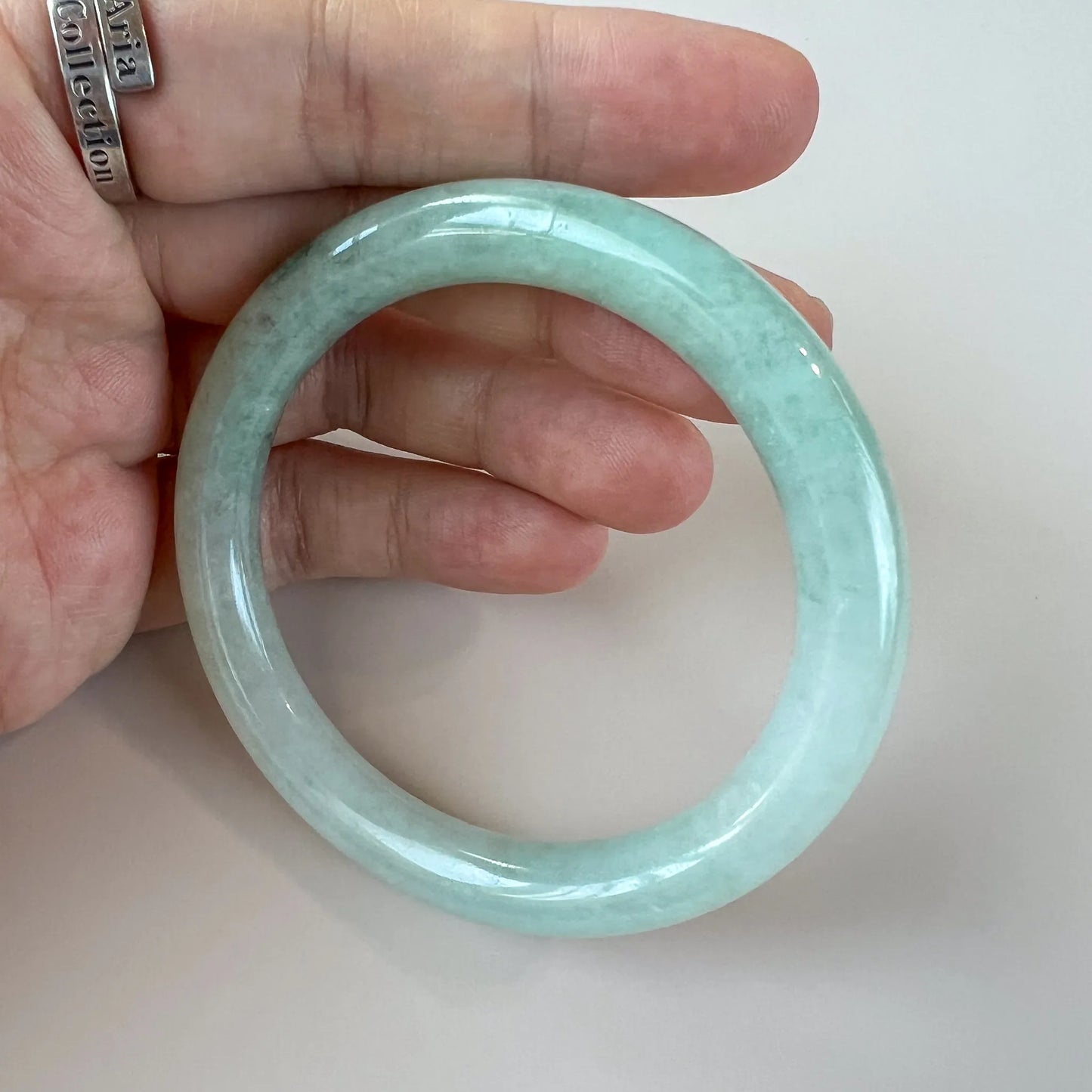 Handheld front view of pale green jade bangle with glossy polish
