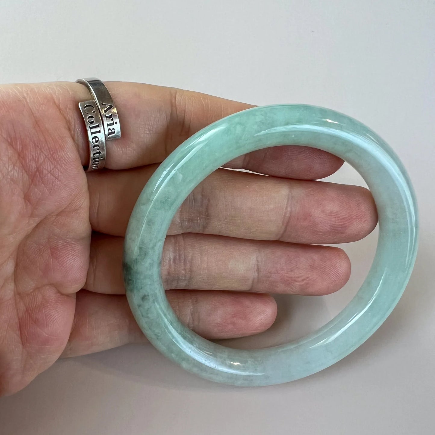 Three-quarter view of polished jade bangle in hand with green marbling