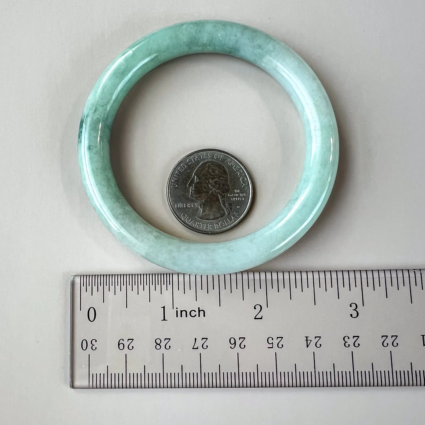 Light green mottled jadeite bangle shown beside a ruler and quarter for size reference