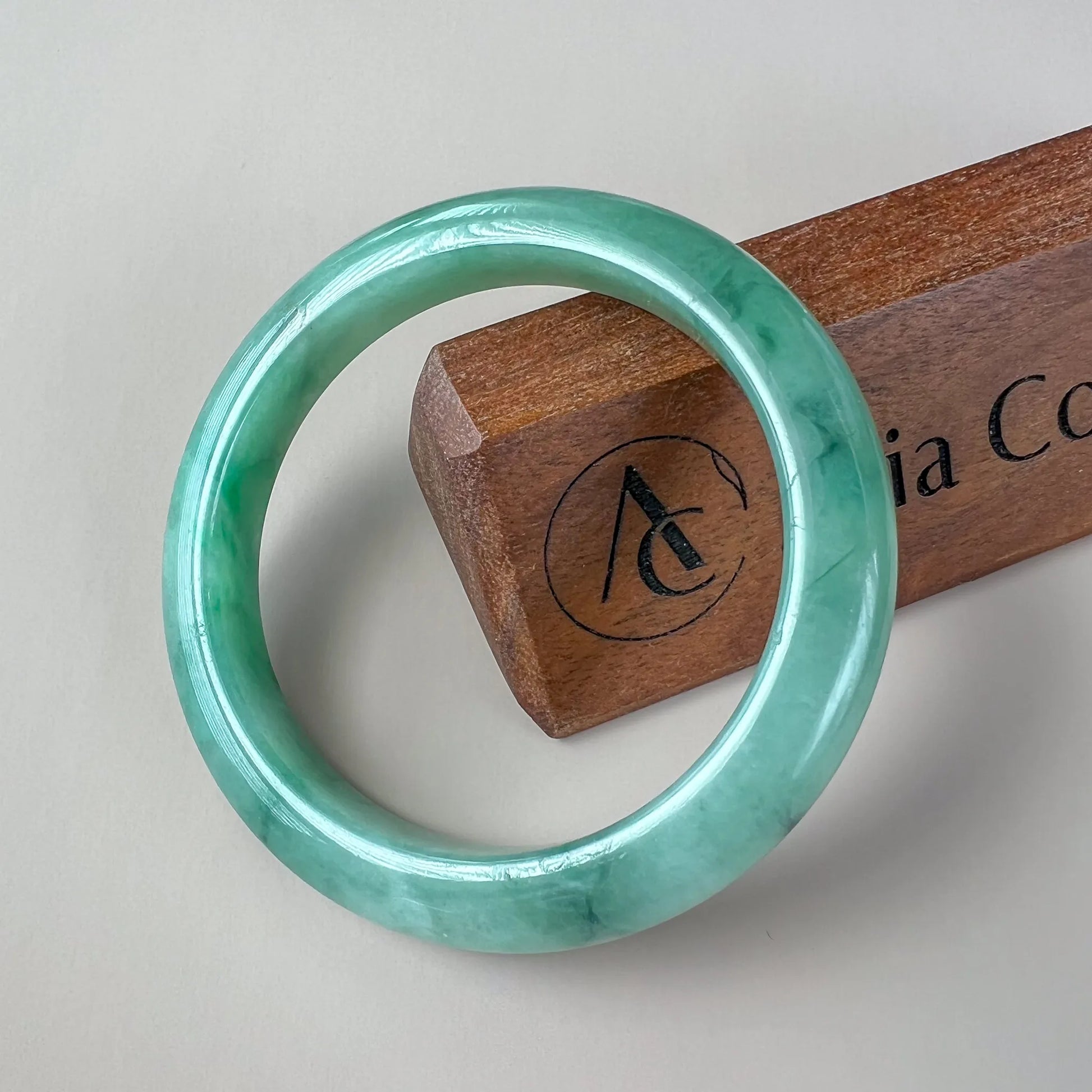 Front view of polished green jade bangle on a wooden display stand