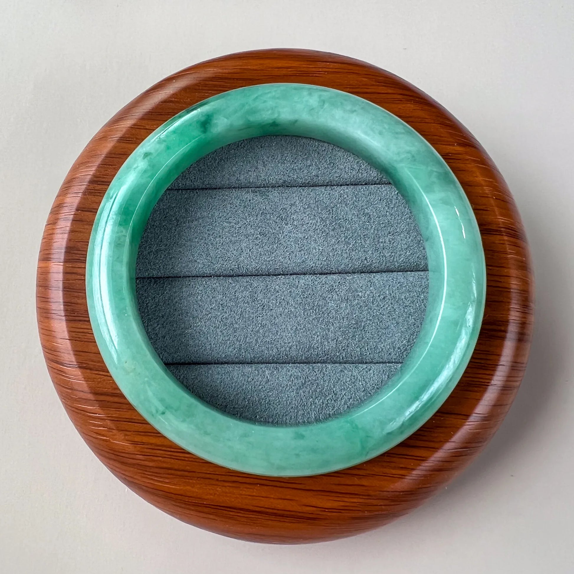 Top view of glossy jade bangle resting on round wood display case