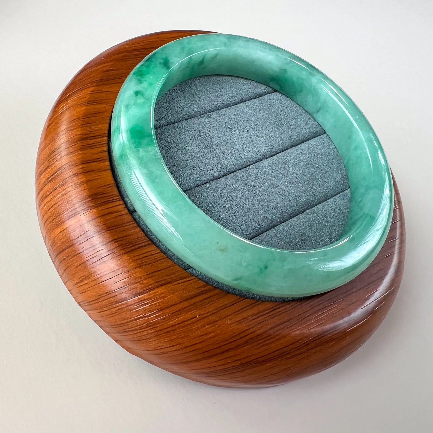 Angled view of smooth green jade bangle on wood stand with padded insert