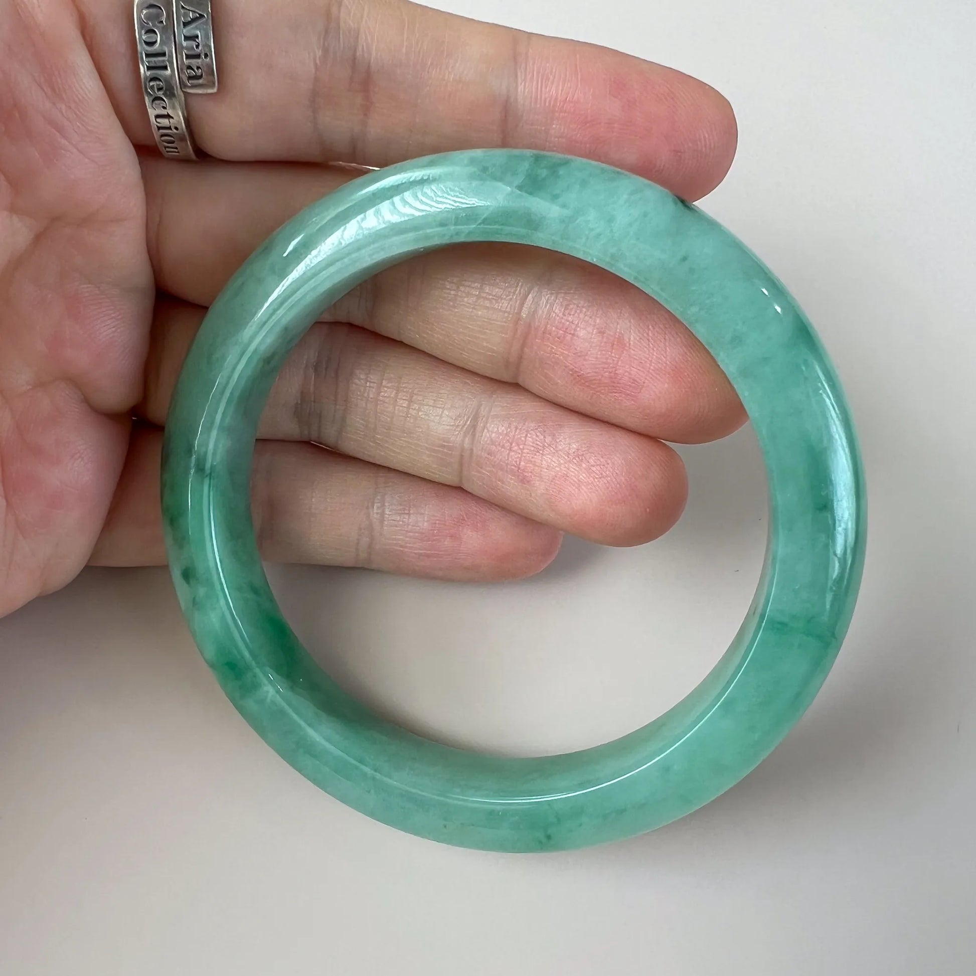Hand-held view of polished green jade bangle showing rounded profile